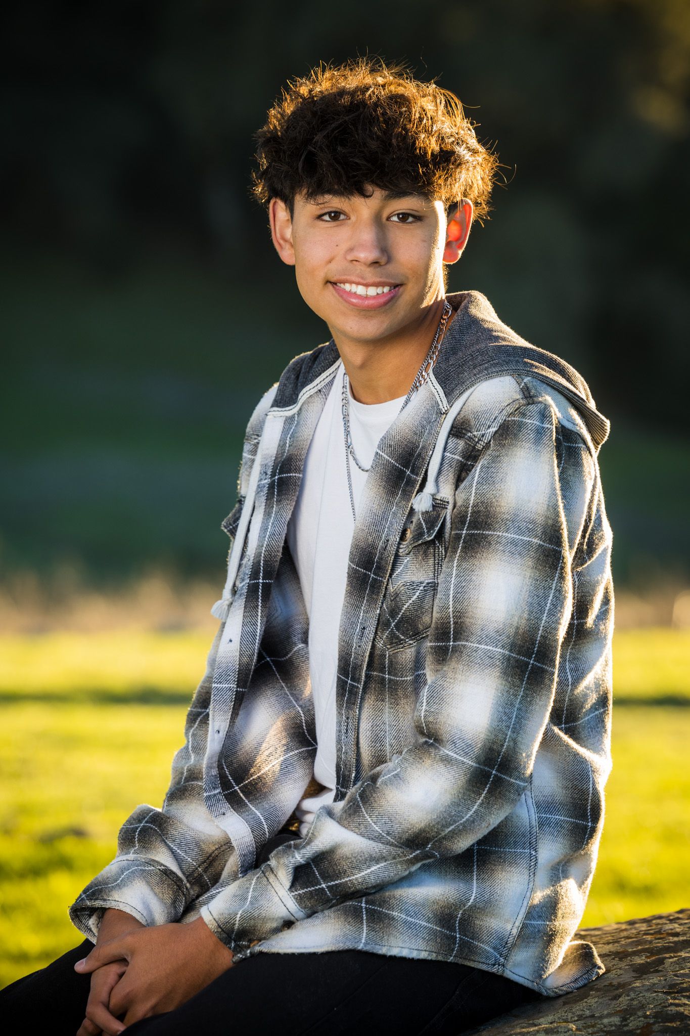 Senior Photos - Outdoor portrait with person wearing plaid jacket sitting in golden hour lighting.