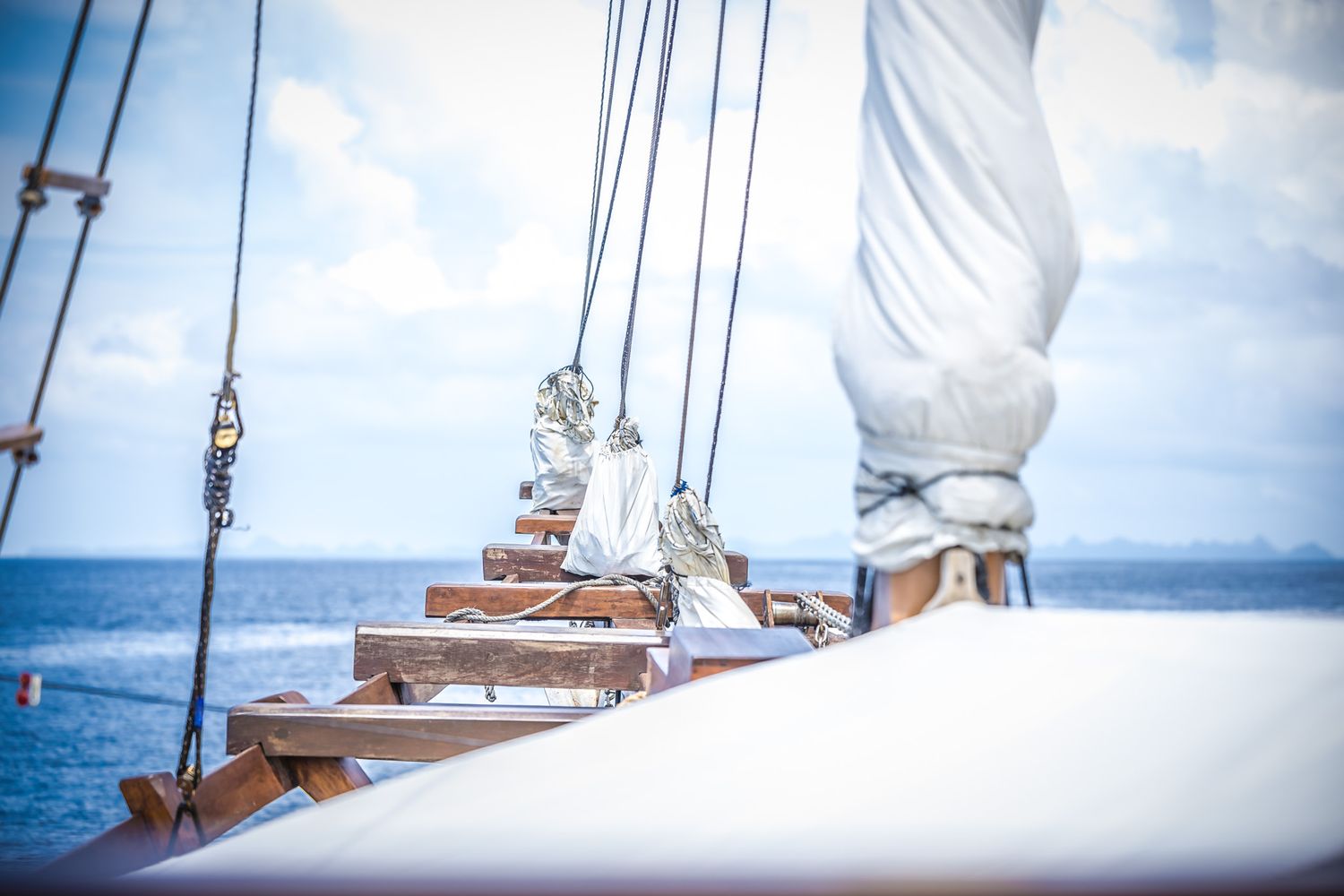 White sails of traditional boat against blue ocean and cloudy sky.
