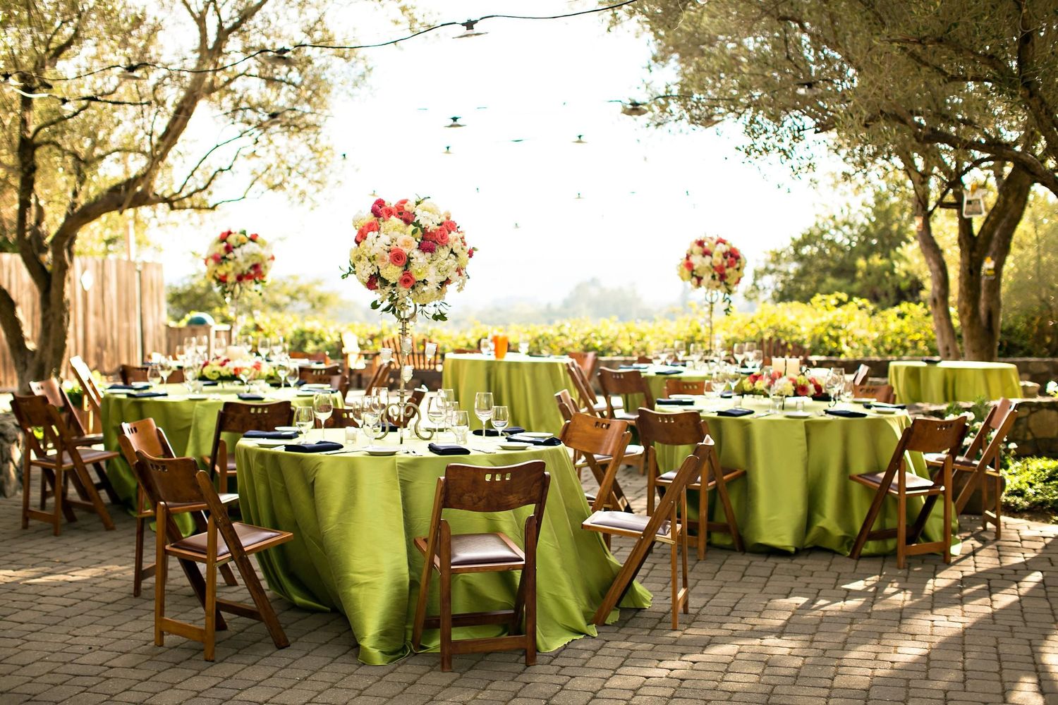 Elegant outdoor wedding reception setup with round tables covered in lime green linens and tall floral centerpieces at sunset.