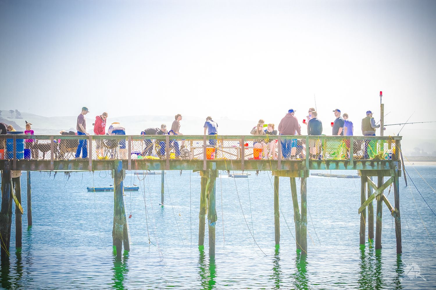People fishing off a wooden pier during sunset over calm waters.