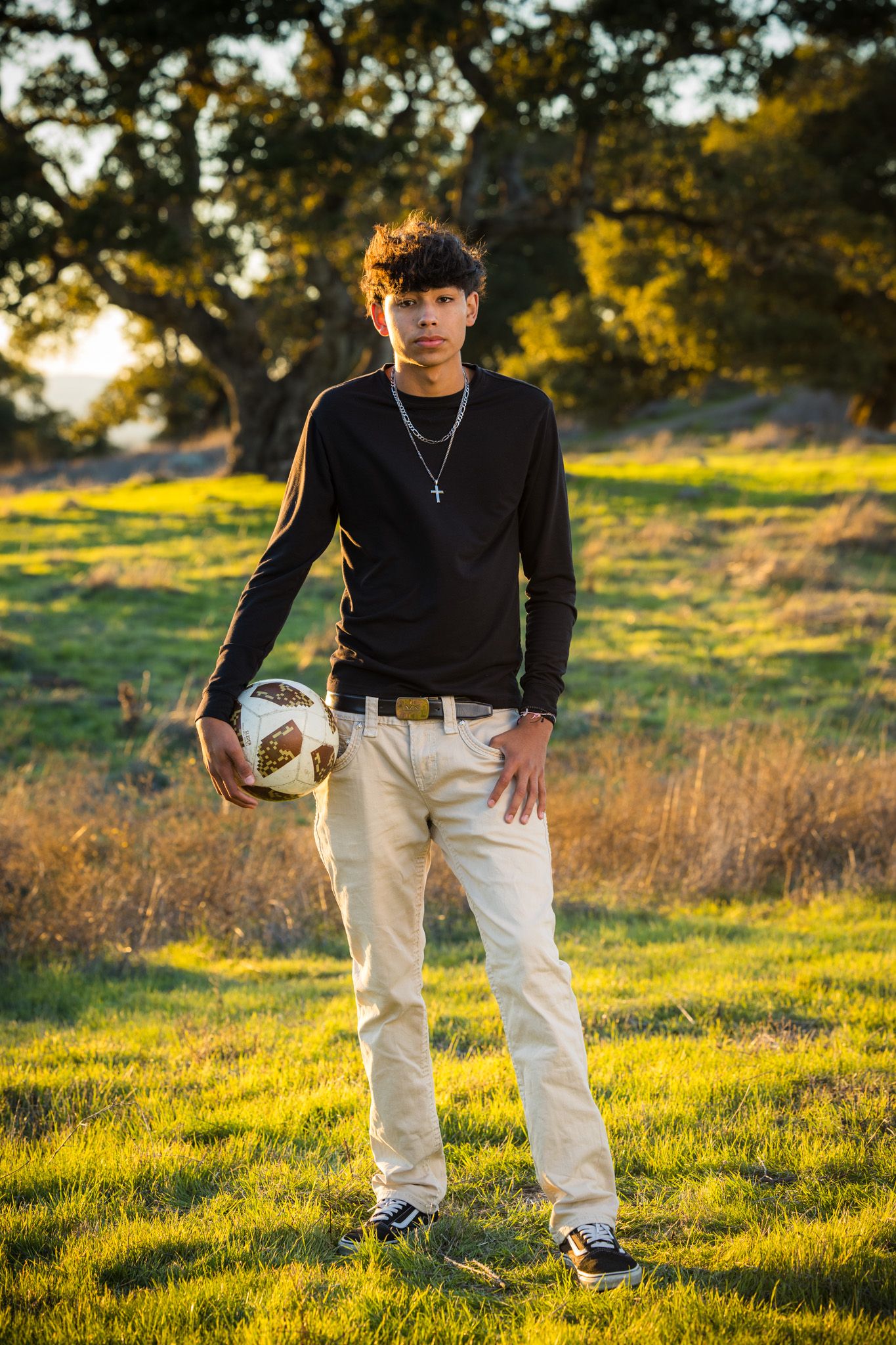 Senior Photos - Figure in black sweater and light pants posed in golden sunlit field.