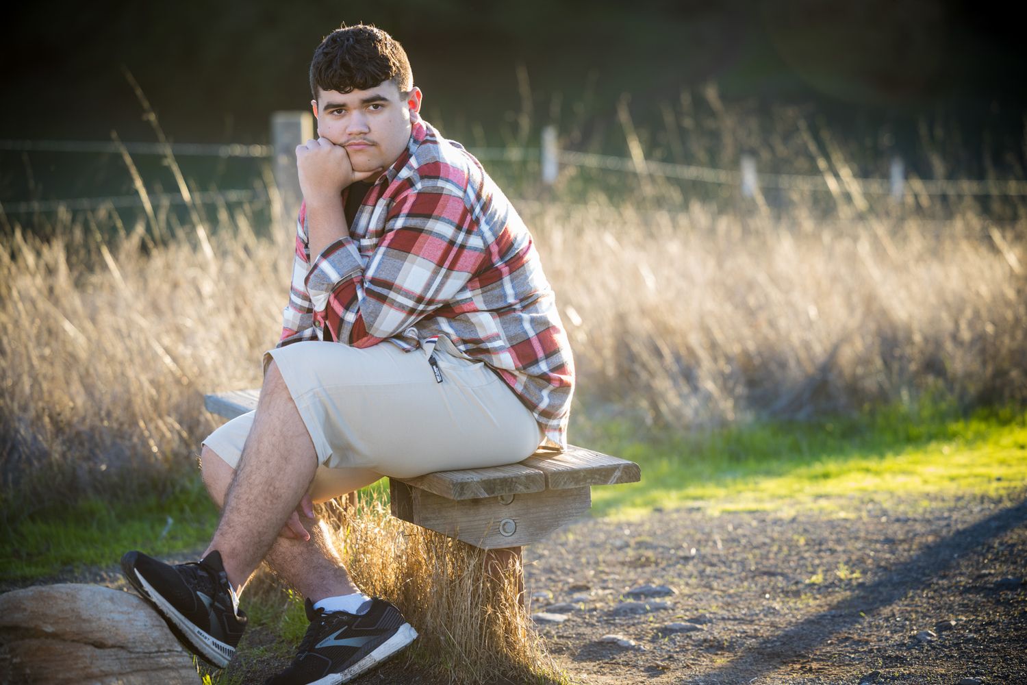 Senior Photos - Person in casual wear sits on wooden stump along dirt path during sunset.