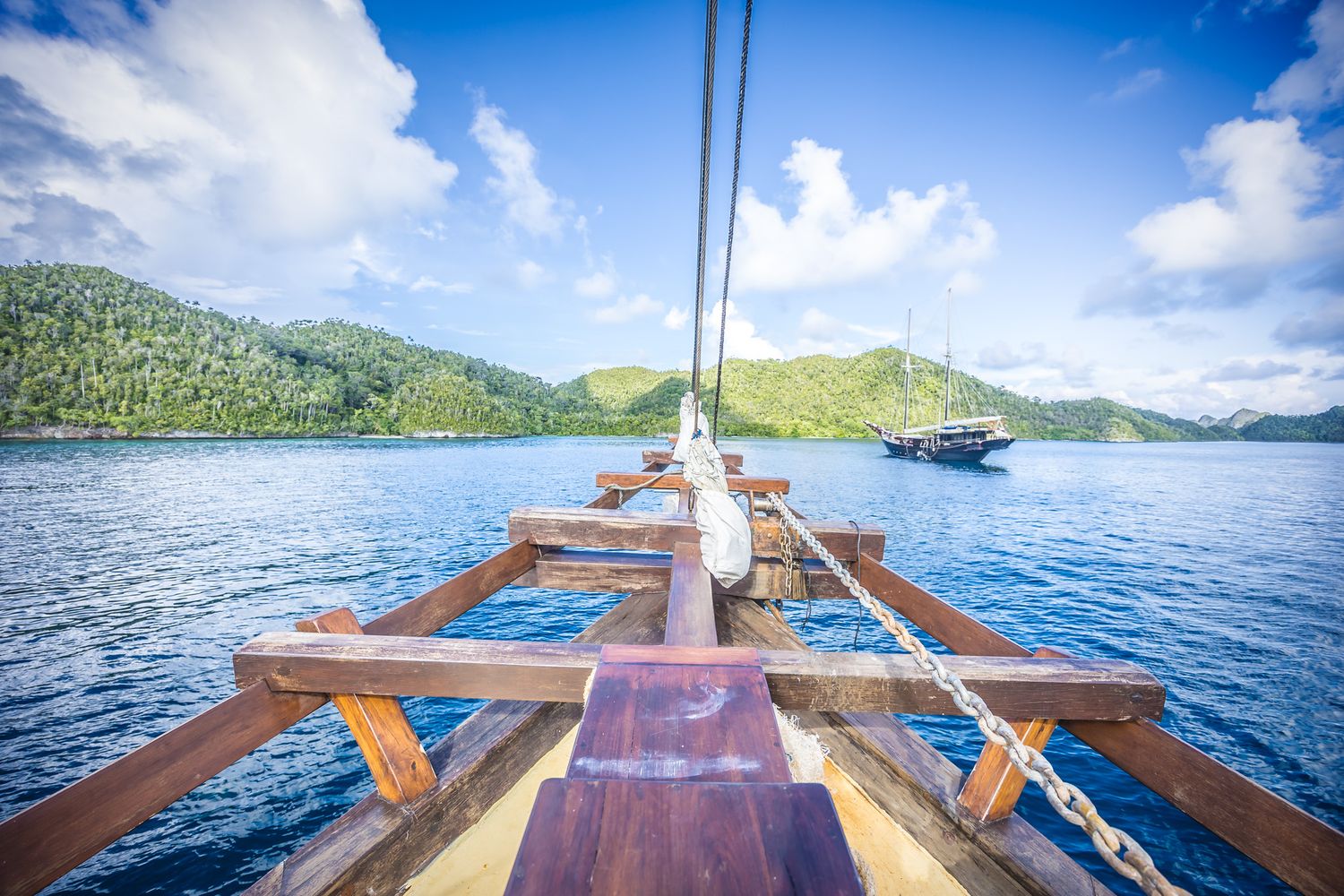 Wooden deck of sailing ship with ocean and tropical islands in background.
