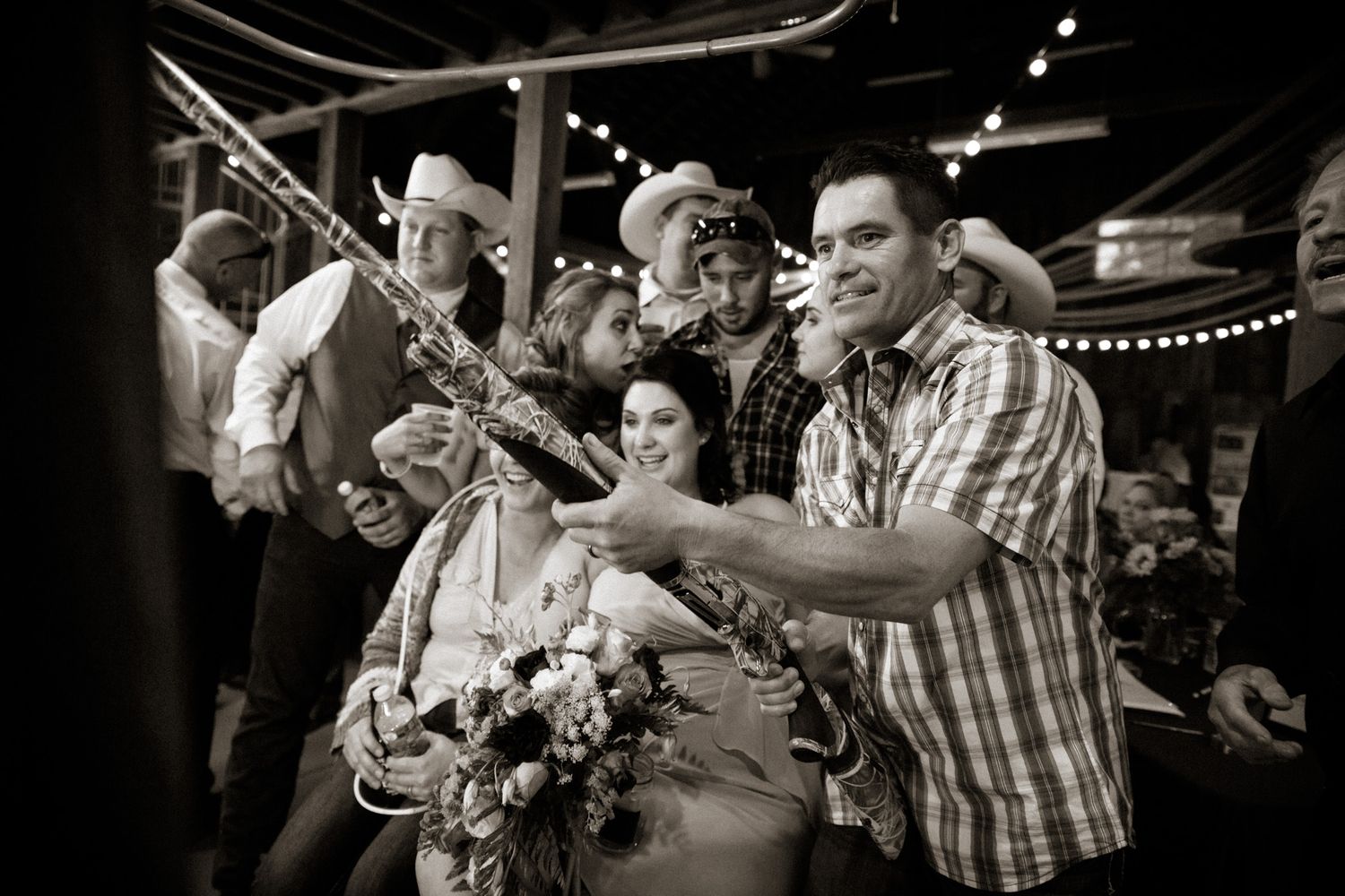 Black and white photo of wedding guests dancing with musical instruments at a lively reception party.