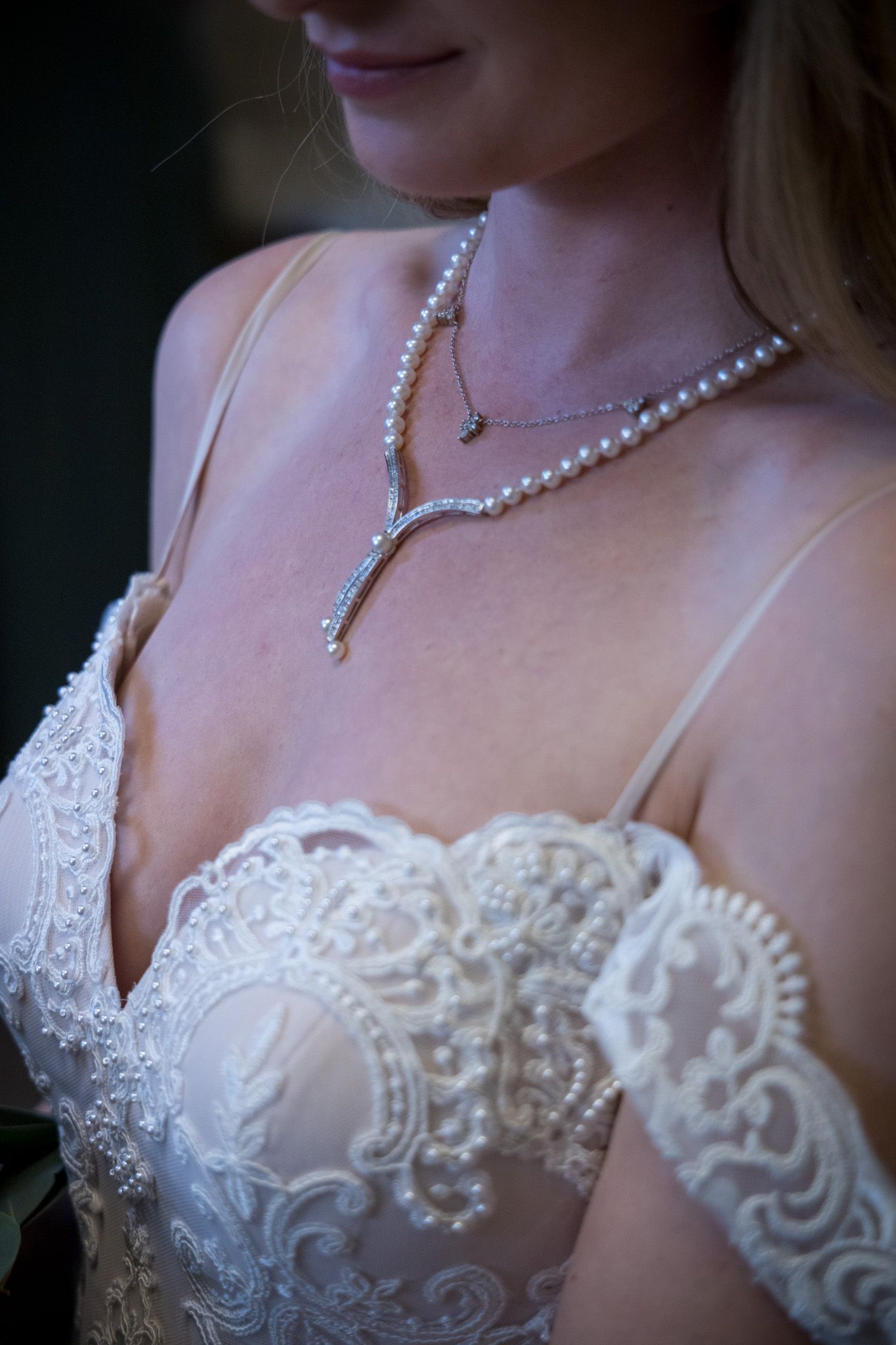 Detail shot of pearl necklace and intricate lace wedding dress bodice.
