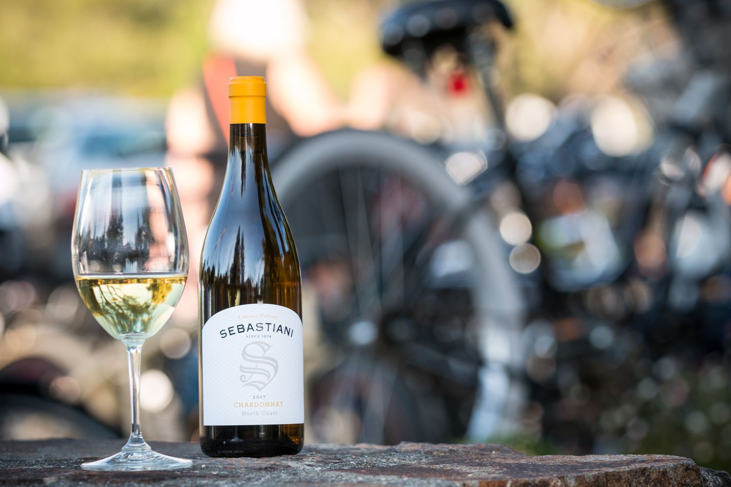 Sebastiani wine bottle and glass of white wine on outdoor table with blurred background.