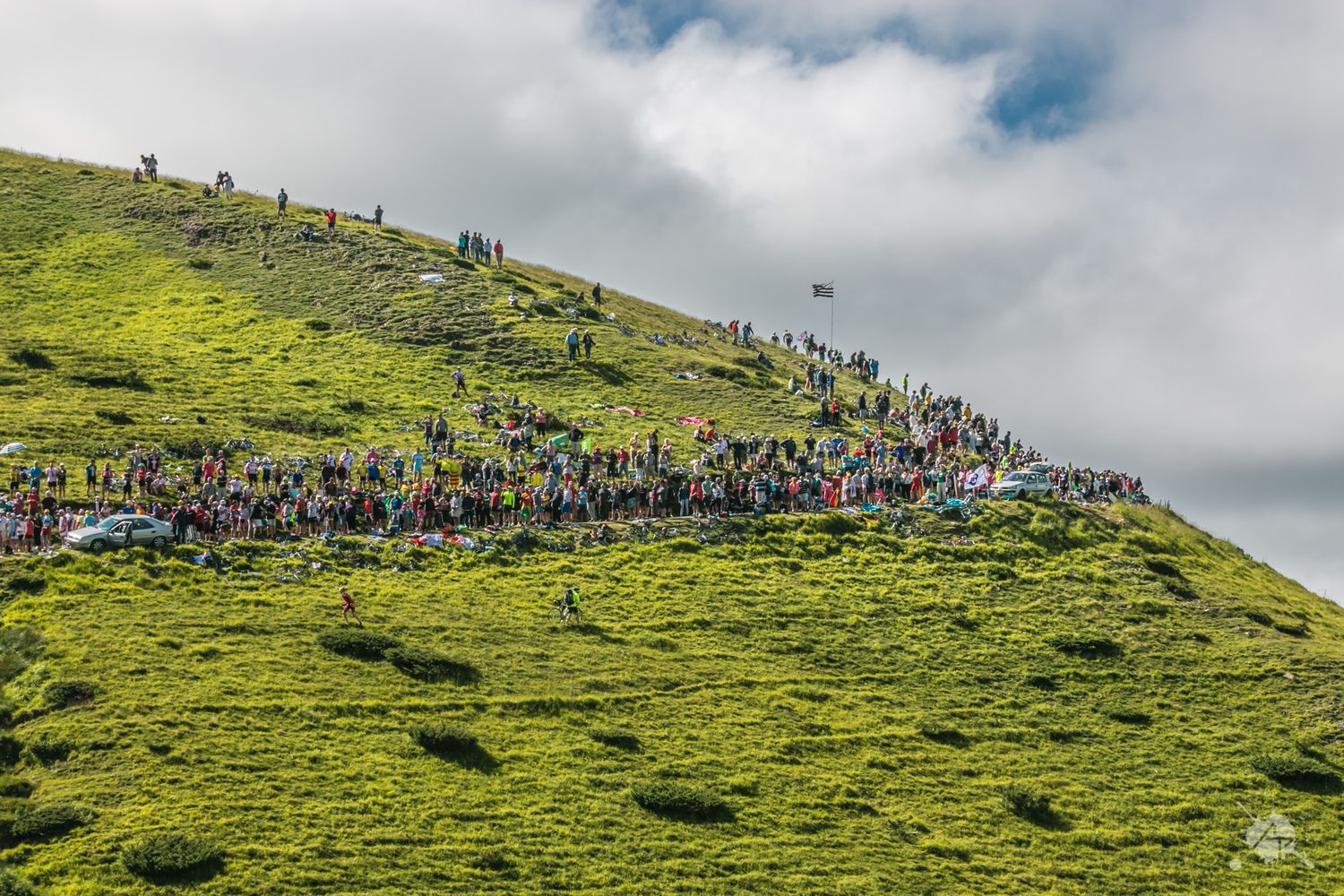 Large crowd of people gathered on green hillside under cloudy sky.