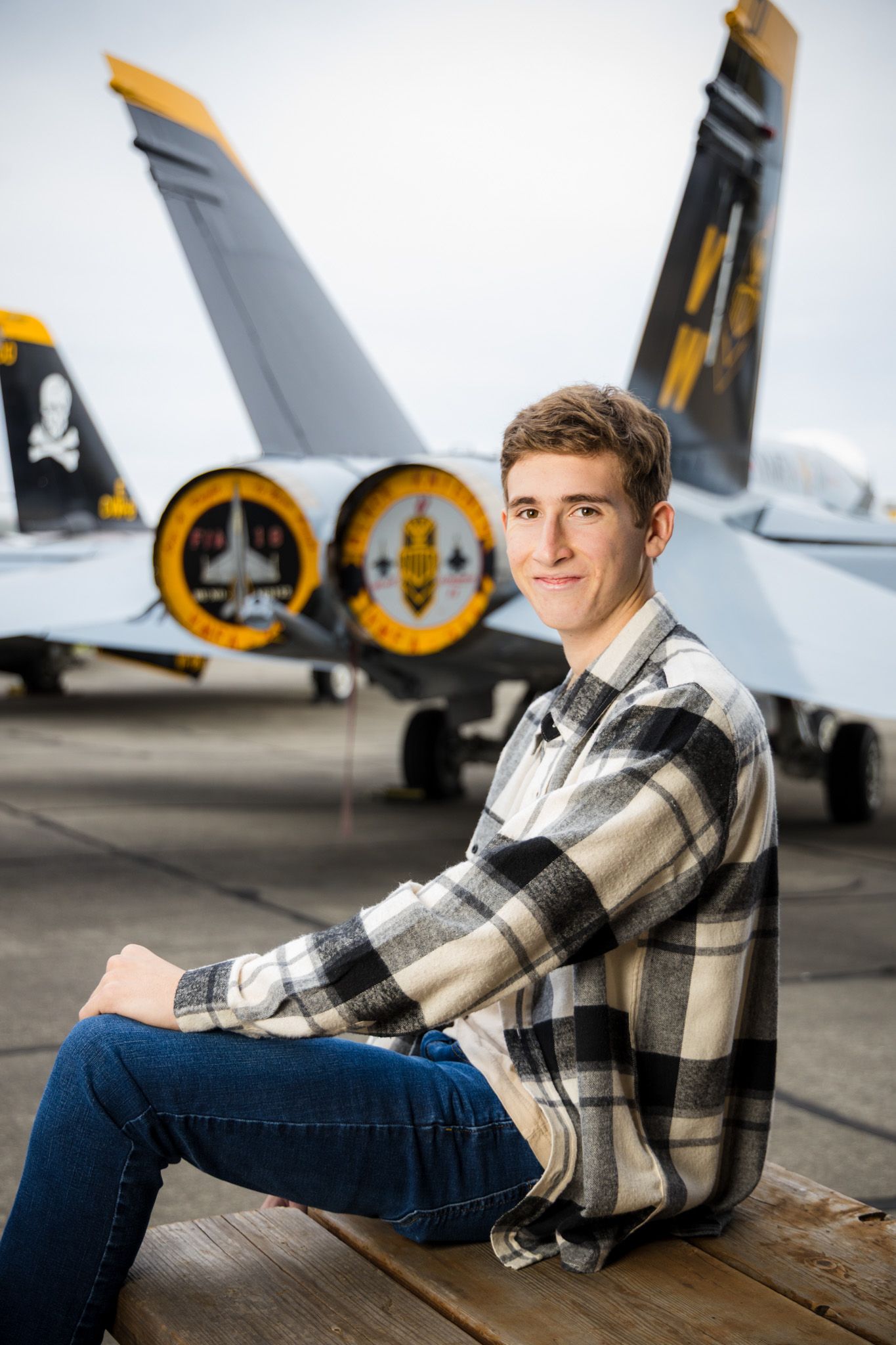 Senior Photos - Aircraft tail fins with military insignia visible behind casual portrait setting.