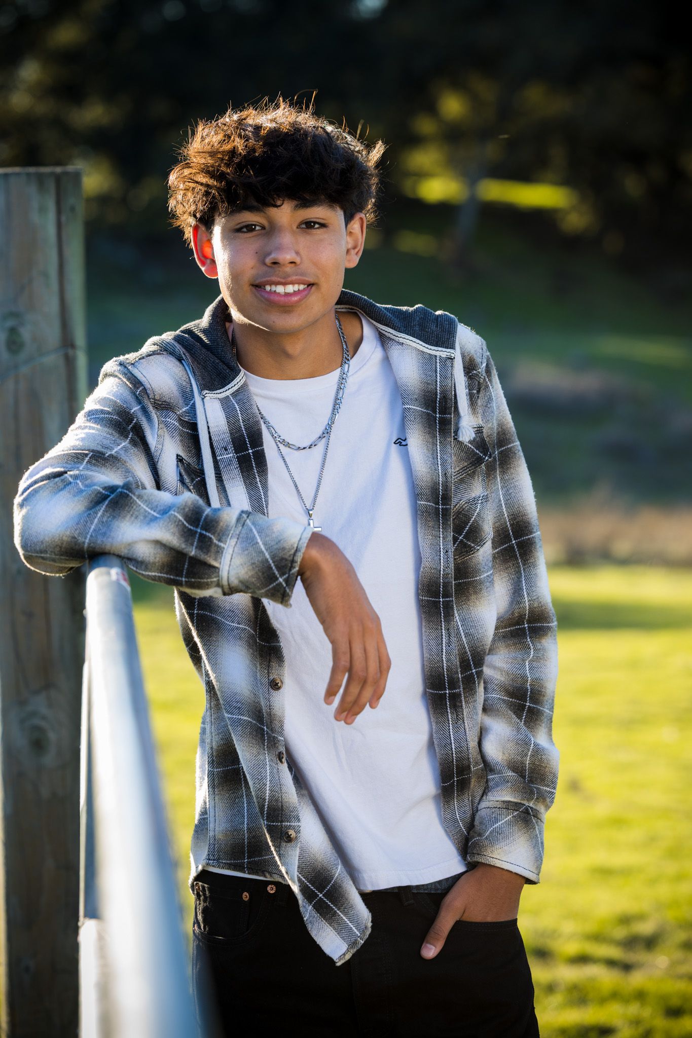Senior Photos - Casual portrait of person in plaid shirt leaning against railing outdoors.