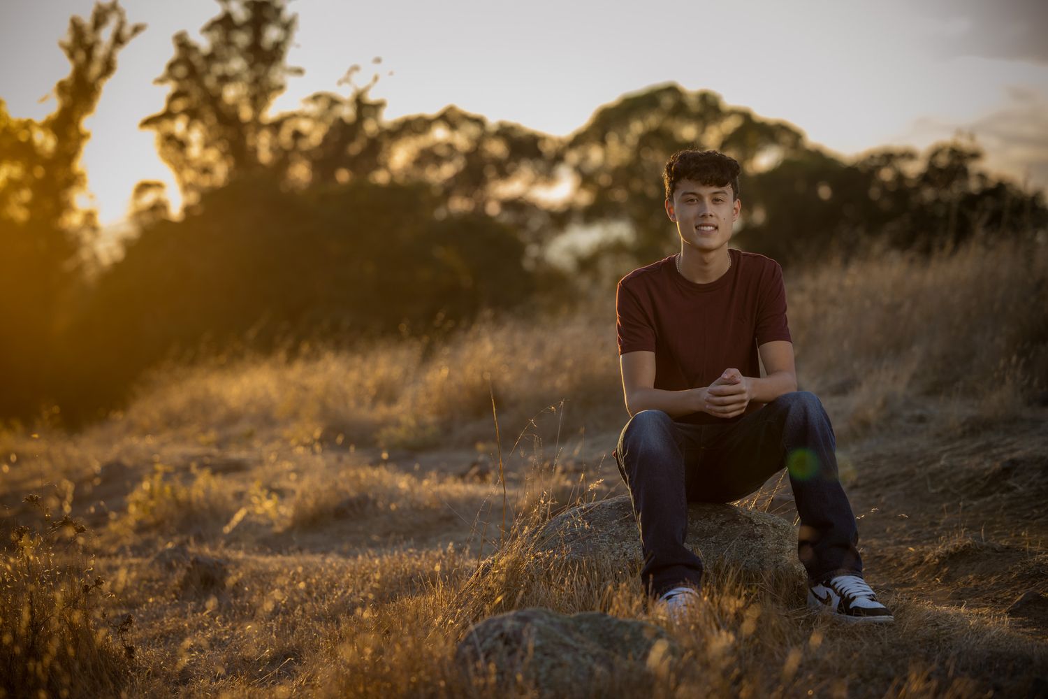 Senior Photos - Outdoor portrait against golden sunset with trees silhouetted in background.