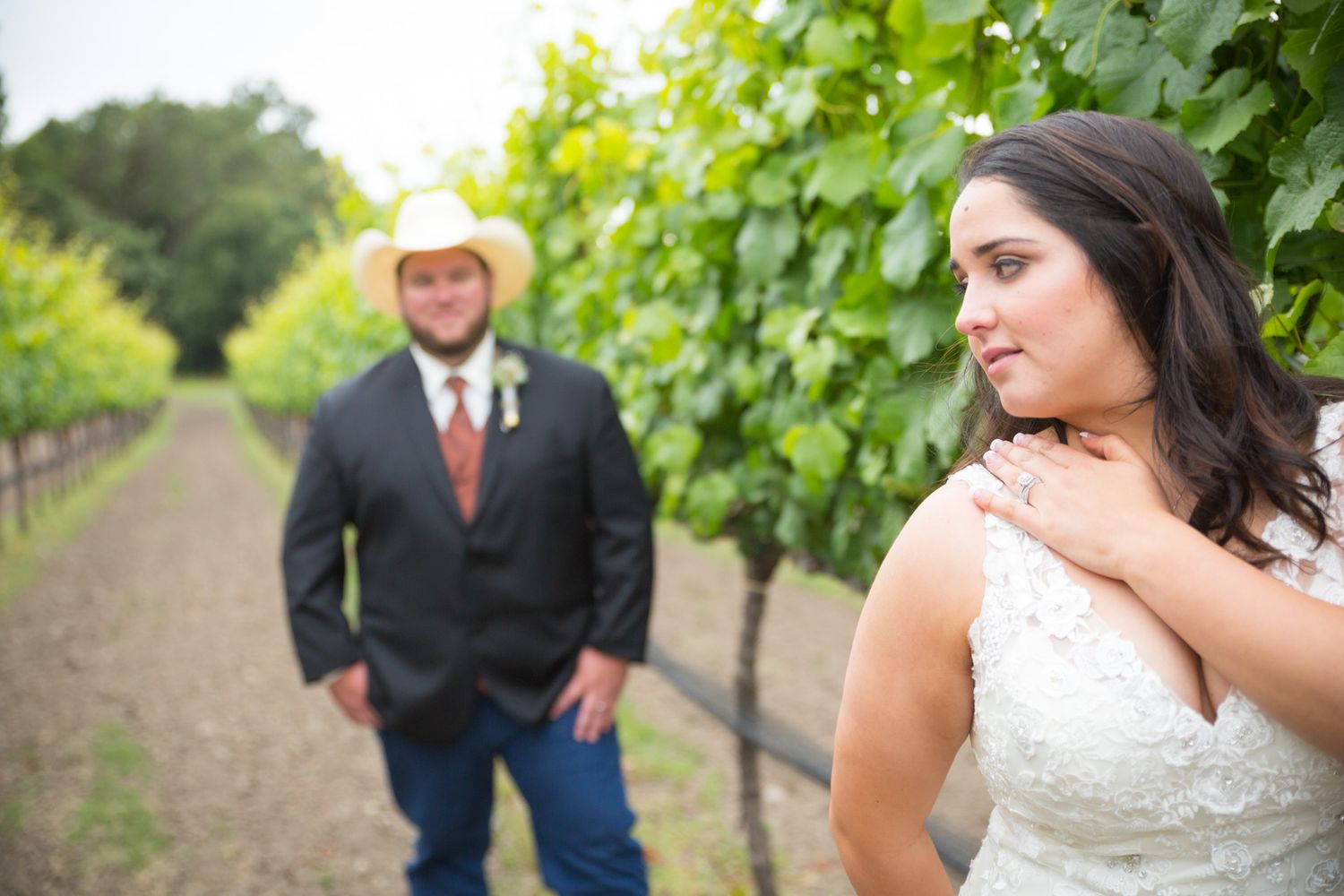 Wedding couple poses amid green vineyard rows for rustic outdoor portrait.
