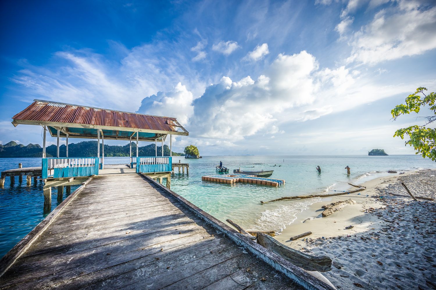 Weathered dock with covered seating area stretches into calm tropical lagoon at low tide.