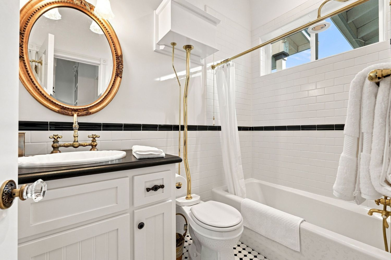 Elegant bathroom with white subway tiles, black accents, gold fixtures, oval mirror, vessel sink, and clawfoot tub.