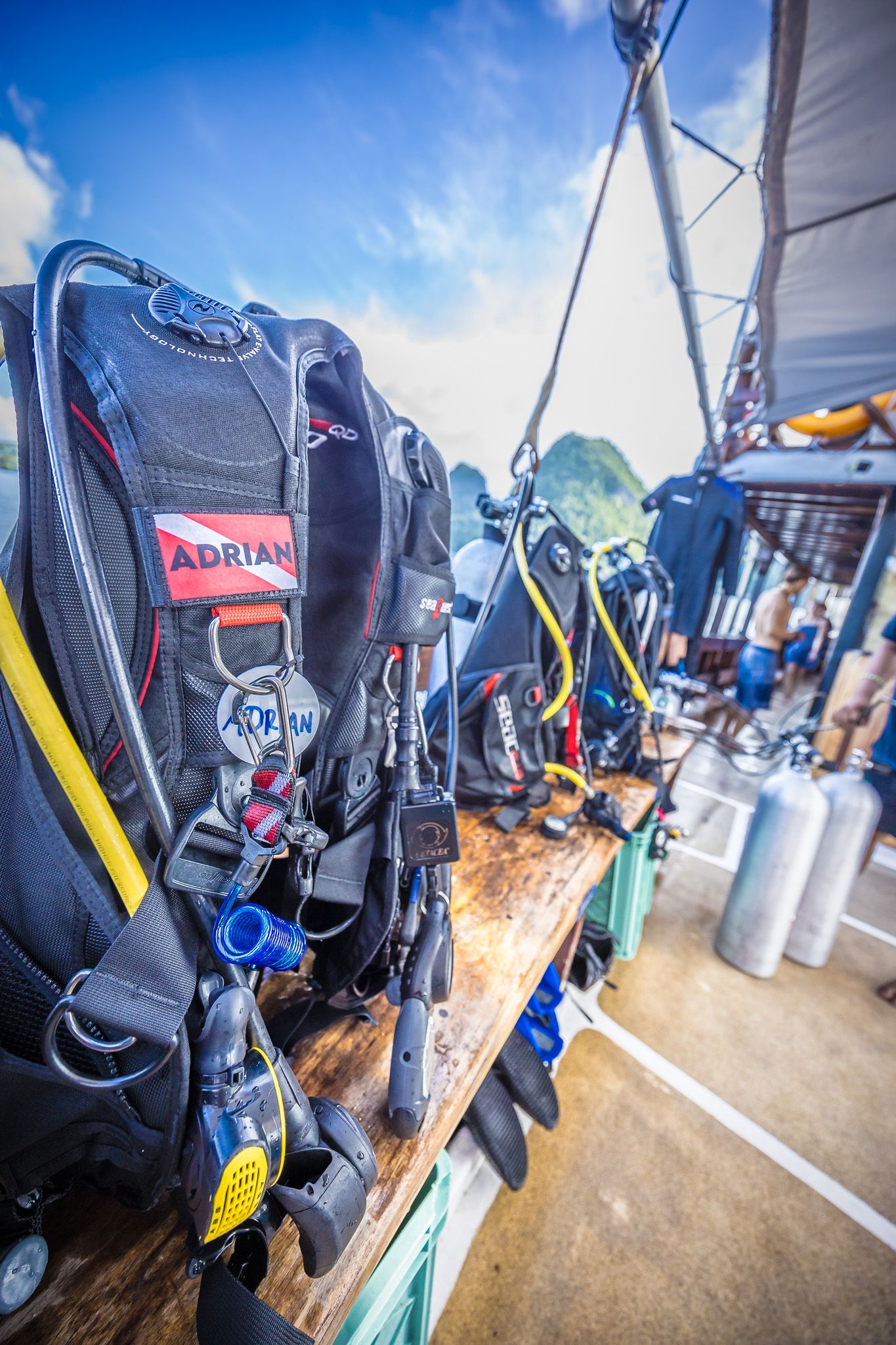 Scuba diving equipment and gear arranged on a boat deck with limestone cliffs visible in background.
