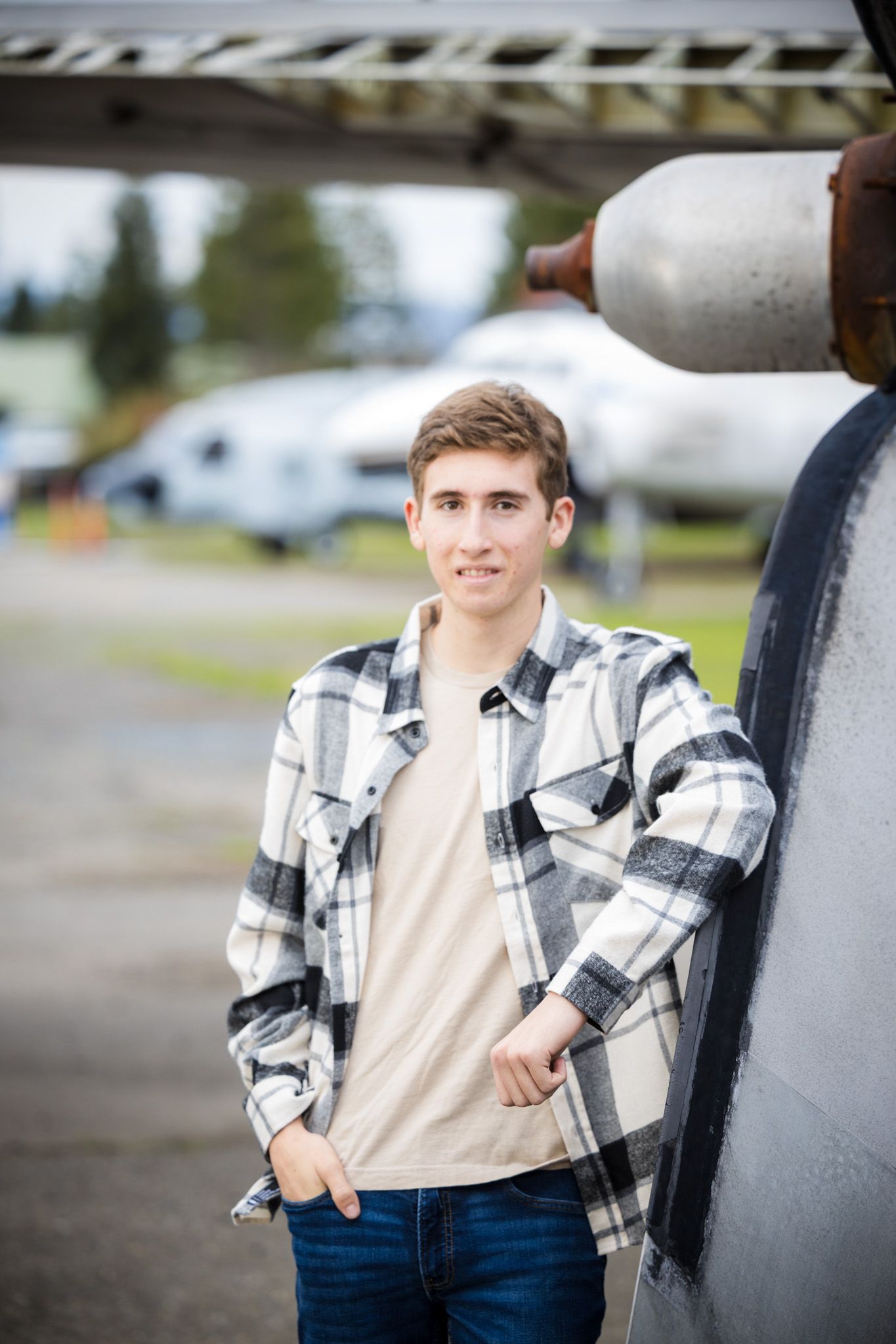 Senior Photos - Casual portrait against aircraft fuselage wearing black and white plaid shirt.