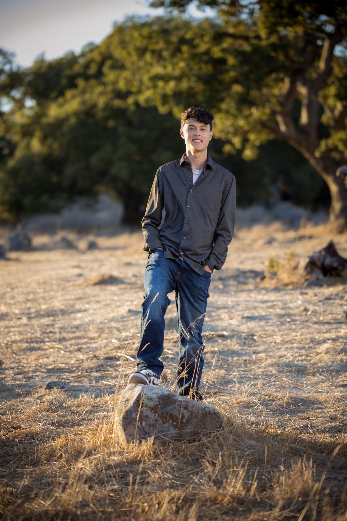 Senior Photos - Casual portrait of a person standing on a rock in a grassy hillside setting.