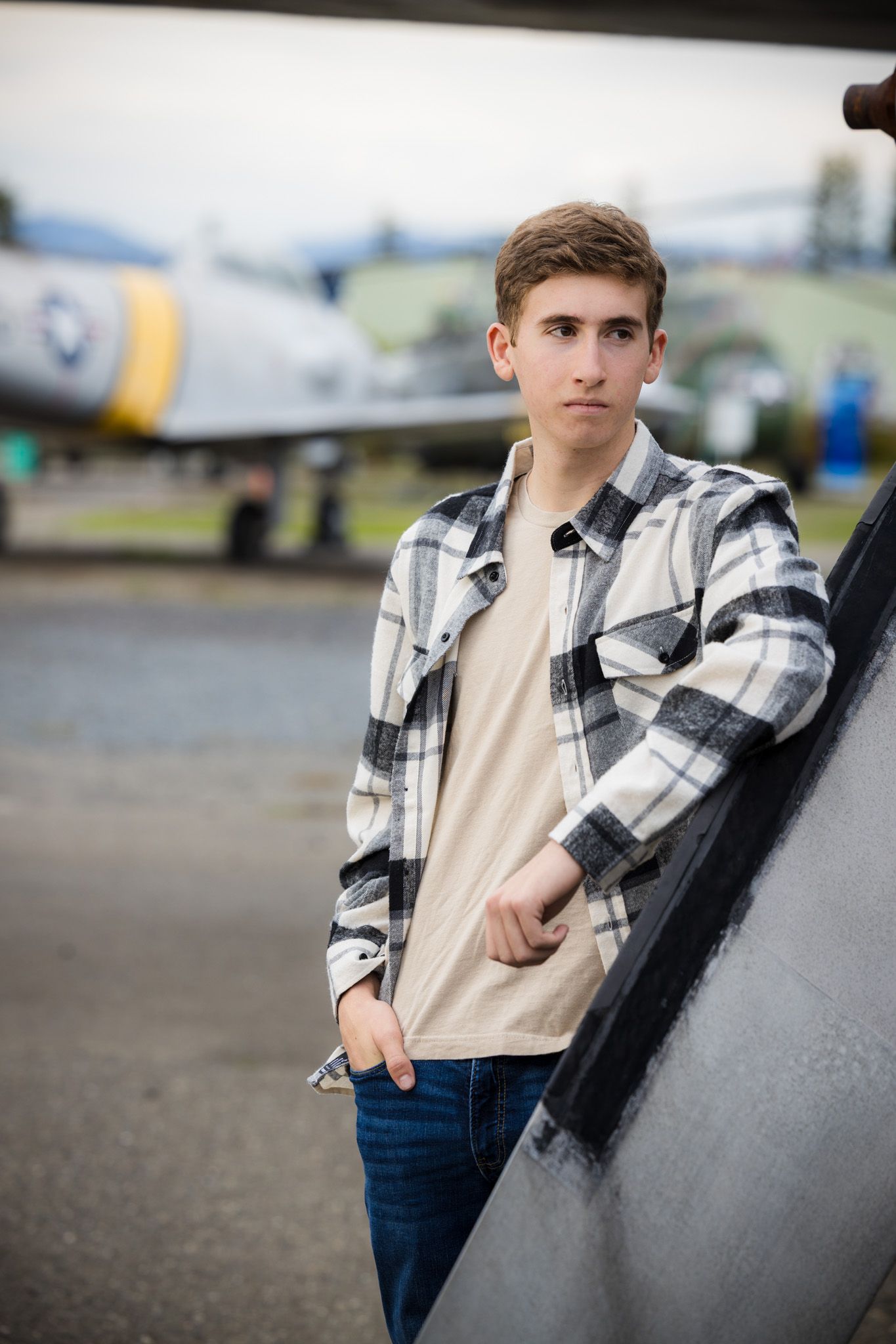Senior Photos - Standing beside vintage aircraft on tarmac wearing plaid flannel shirt and jeans.