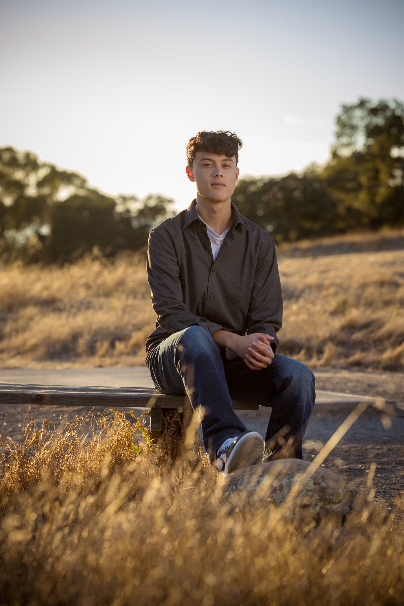 Senior Photos -Lifestyle portrait of someone sitting on a bench in dry grass during sunset.