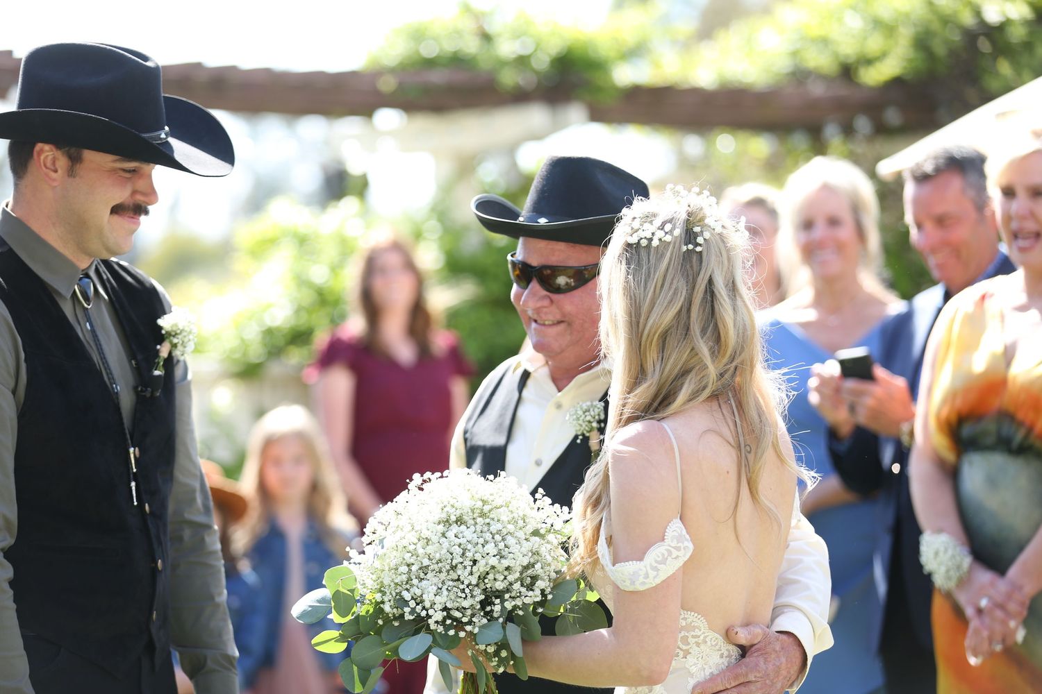 Couple at an outdoor wedding ceremony exchanging vows with officiant and guests in garden setting.