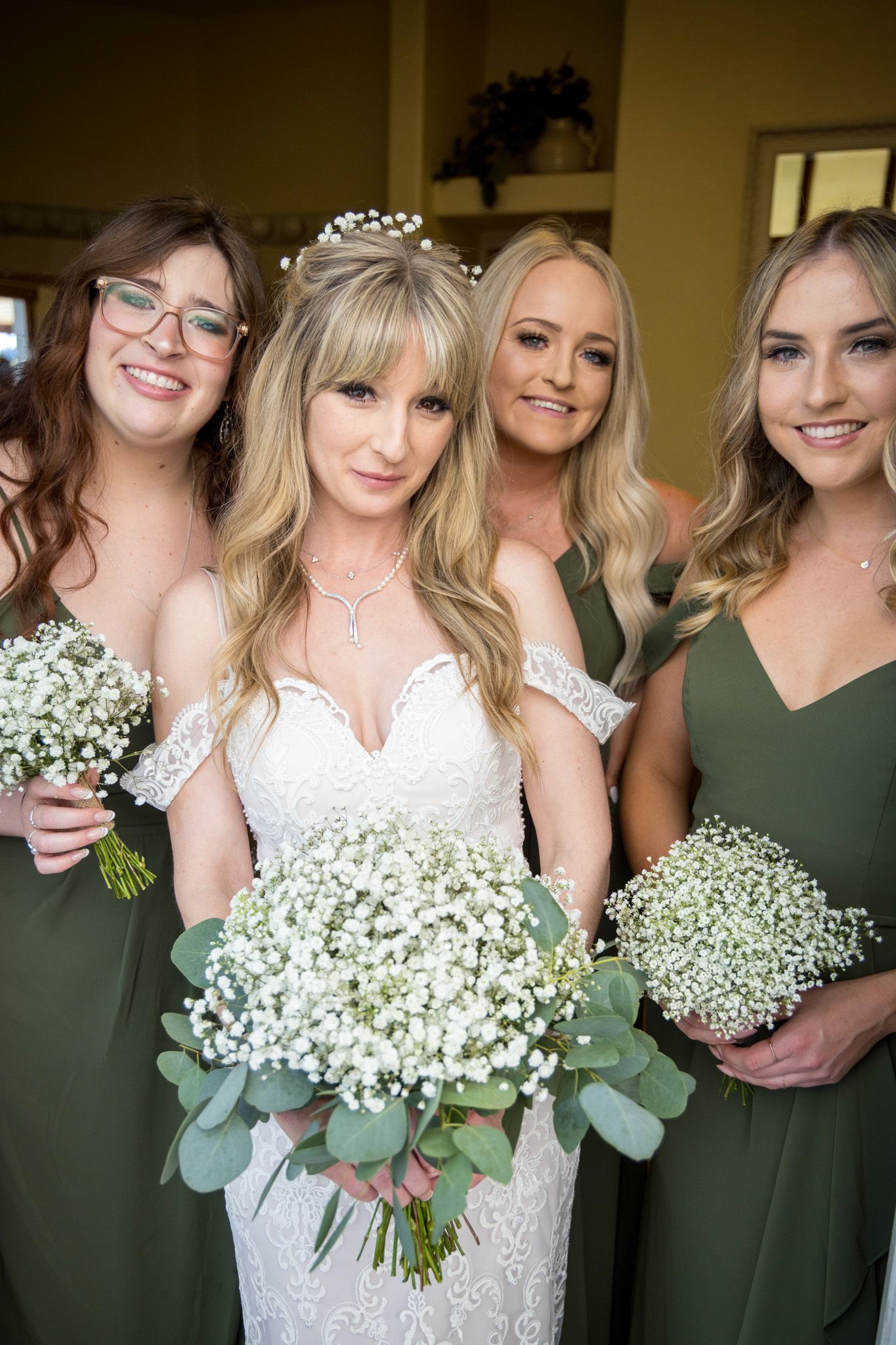 Wedding party photo with bridesmaids in sage green dresses holding baby's breath bouquets alongside the bride.