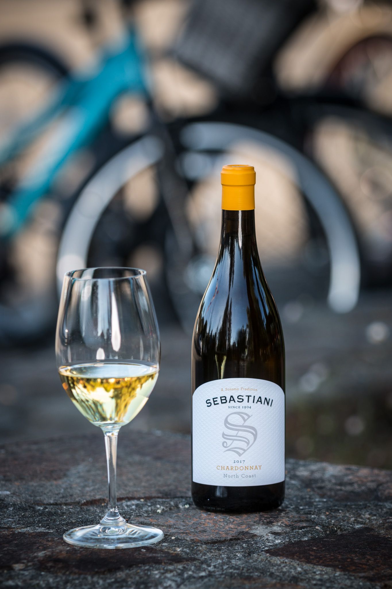 Sebastiani white wine bottle and filled wine glass against blurred bicycle background.