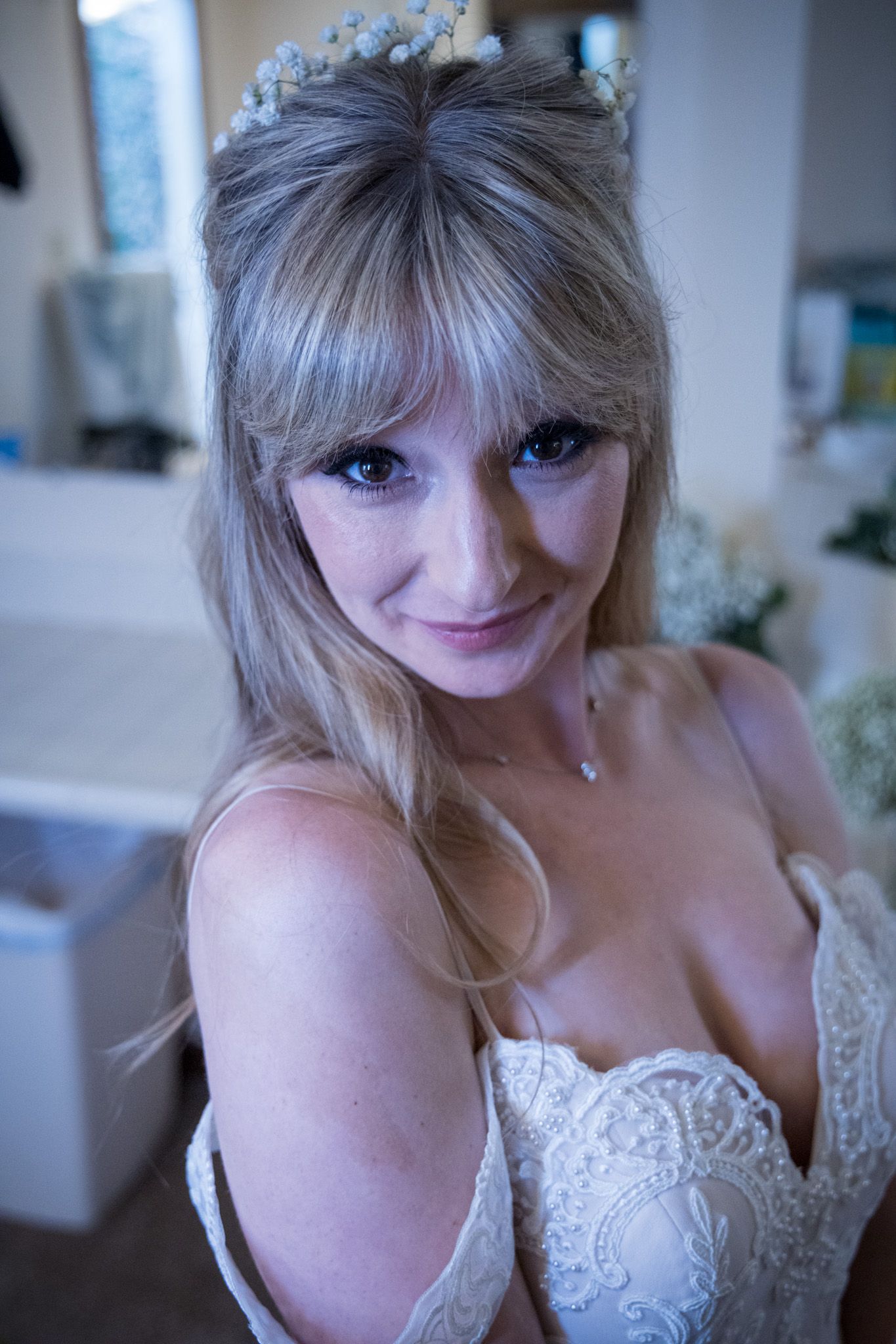 A bride wearing a white lace wedding dress and delicate floral crown smiles at the camera.