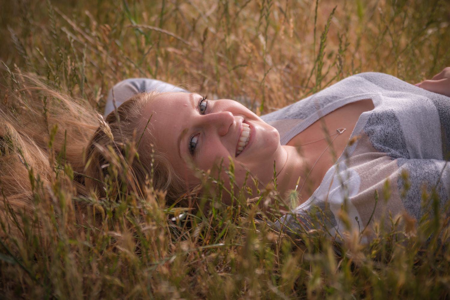 A dreamy portrait of someone lying in tall golden grass with a joyful expression.