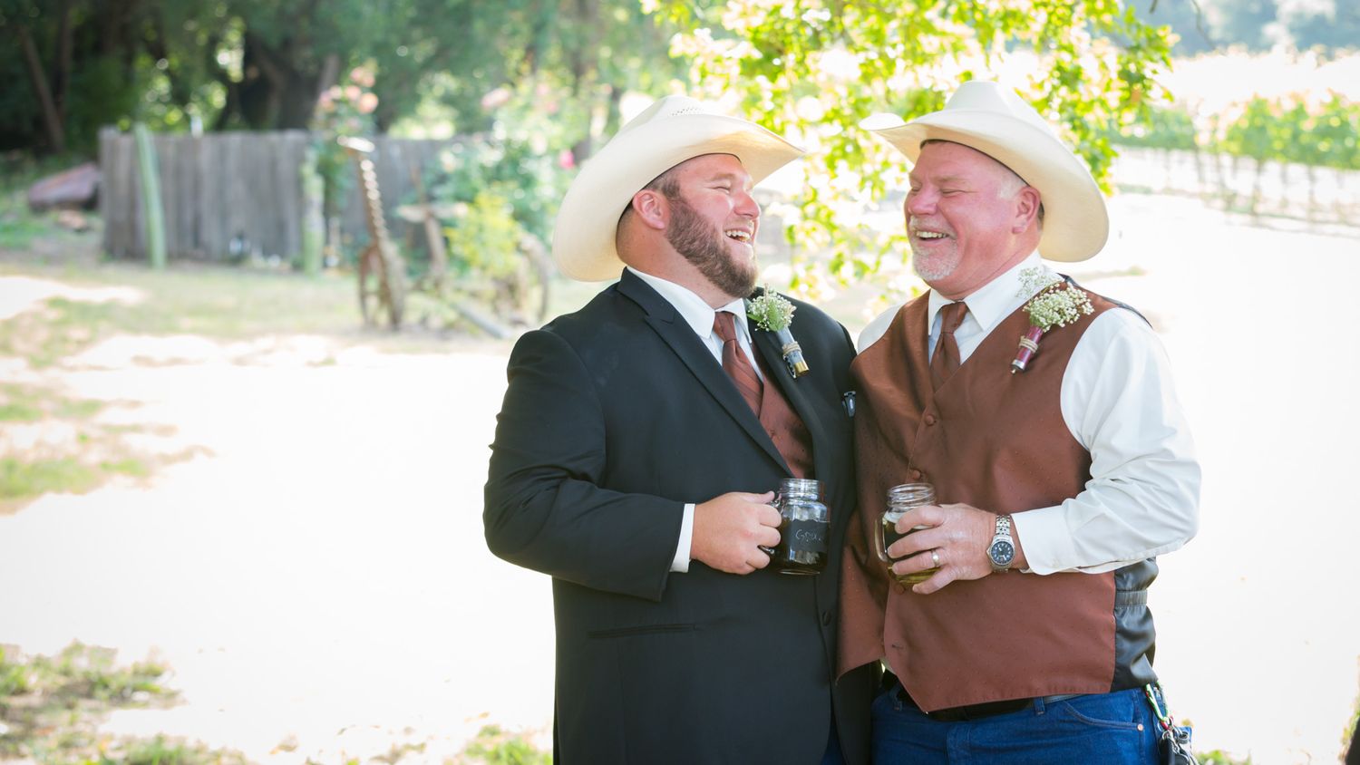 Two people in western attire share a laugh while holding drinks at an outdoor celebration.