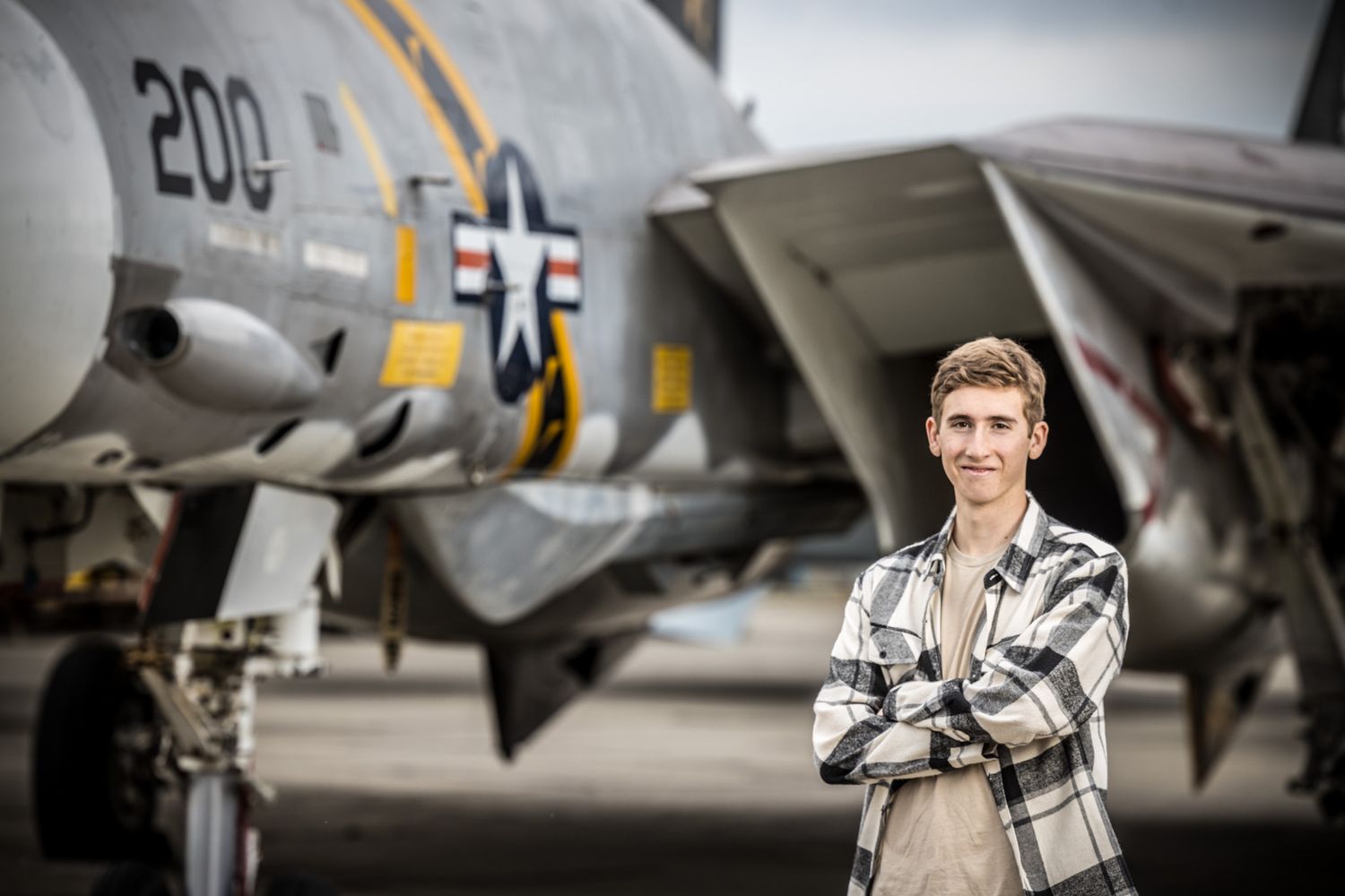 Senior Photos - Standing with crossed arms beside vintage military aircraft tail number 200.
