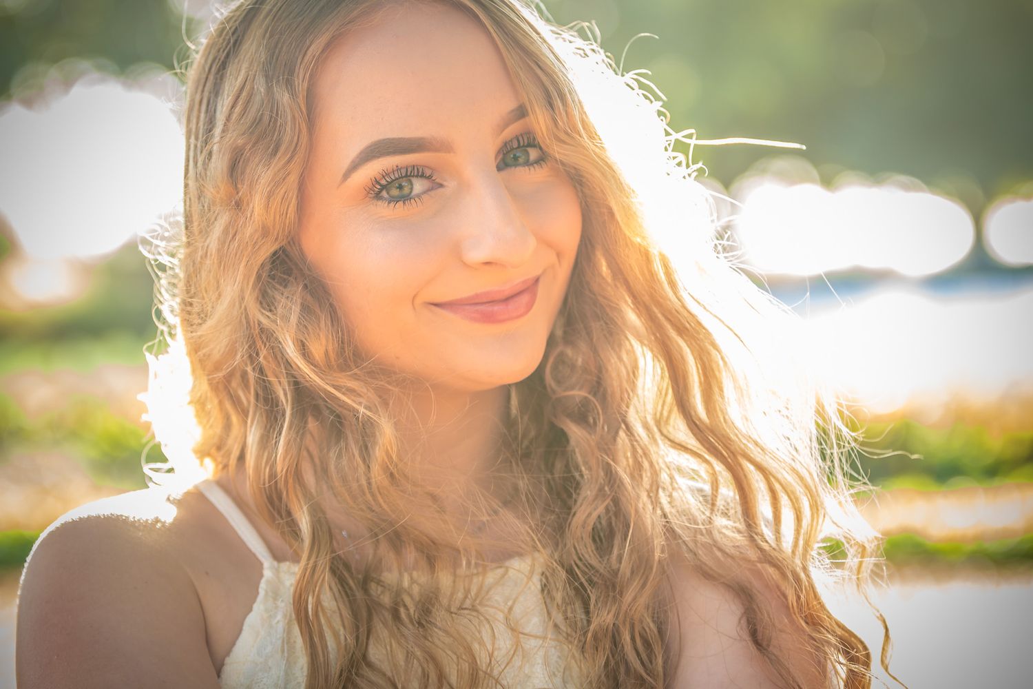 Sunlit portrait of a young woman with wavy blonde hair smiling warmly on a bright summer day.