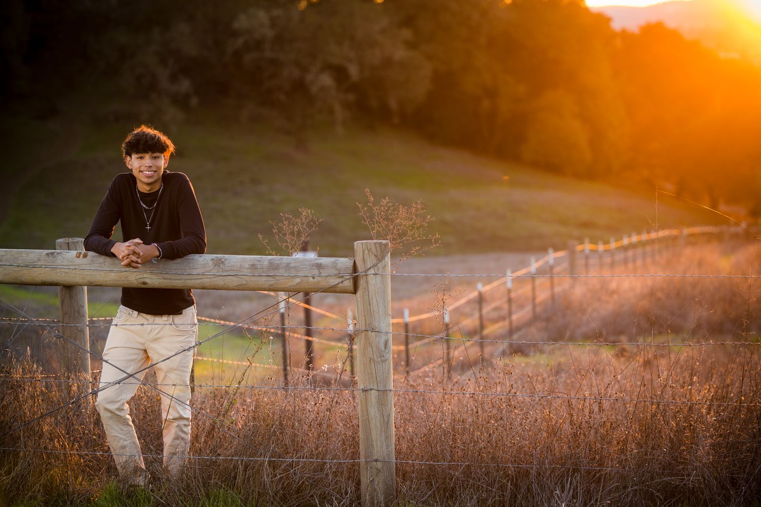 Senior Photos - Panoramic sunset view with wooden fence and figure silhouetted against orange sky.