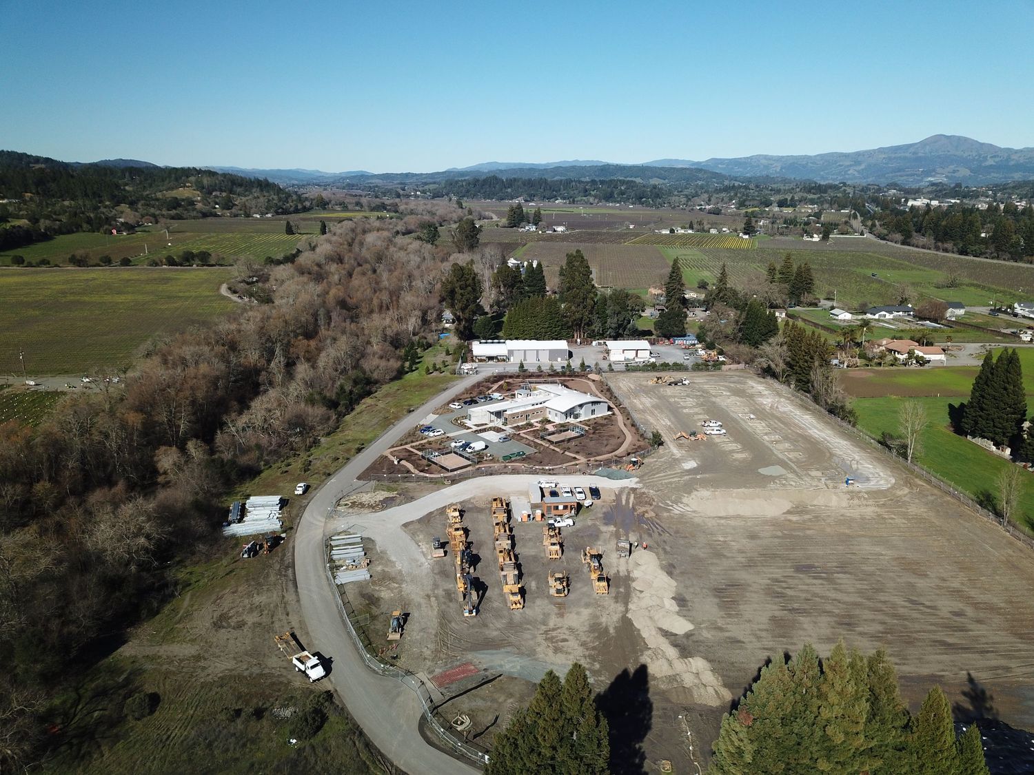 Aerial view of a construction site surrounded by rural landscape and mountains.