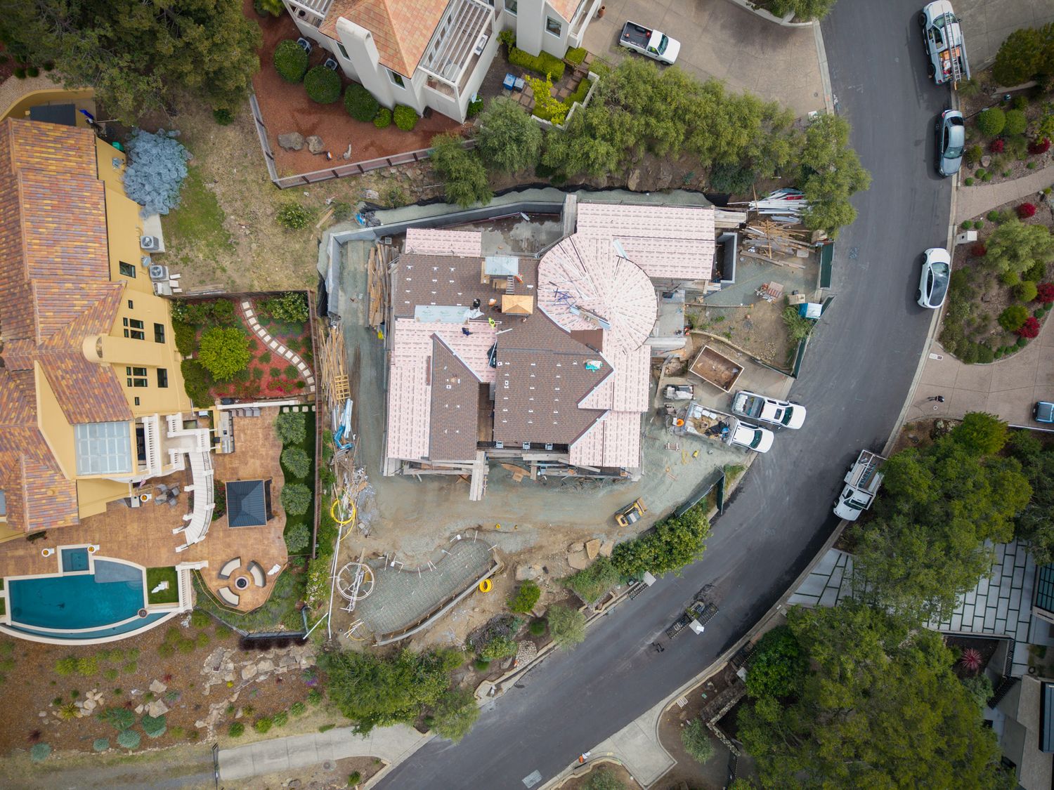 Aerial drone view of a hillside residential neighborhood with curved road, tile-roof homes, and lush trees in California.