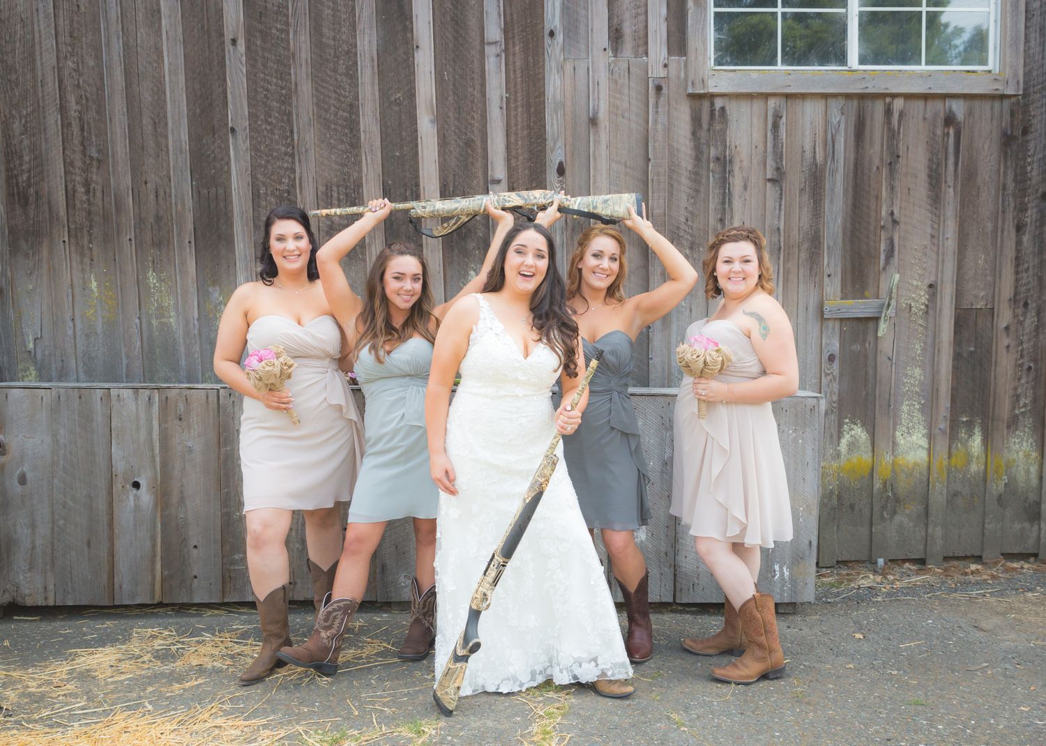 A bridal party wearing cowboy boots poses against a rustic barn wall during a country wedding celebration.