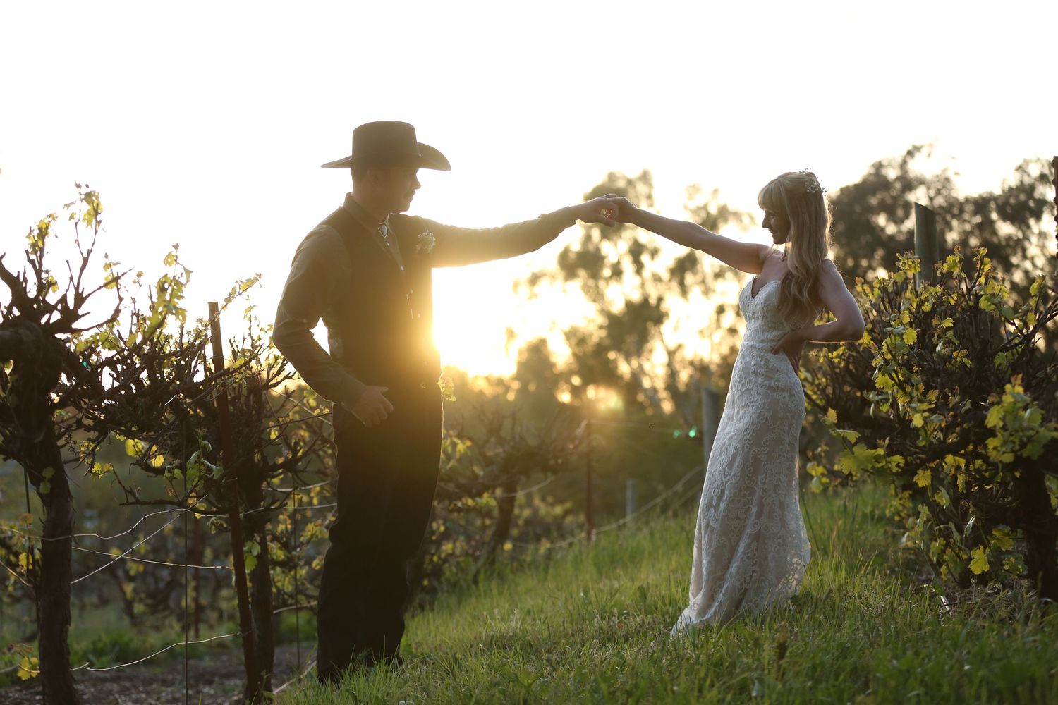 A couple dancing together at sunset in a vineyard, with golden sunlight streaming through the vines.