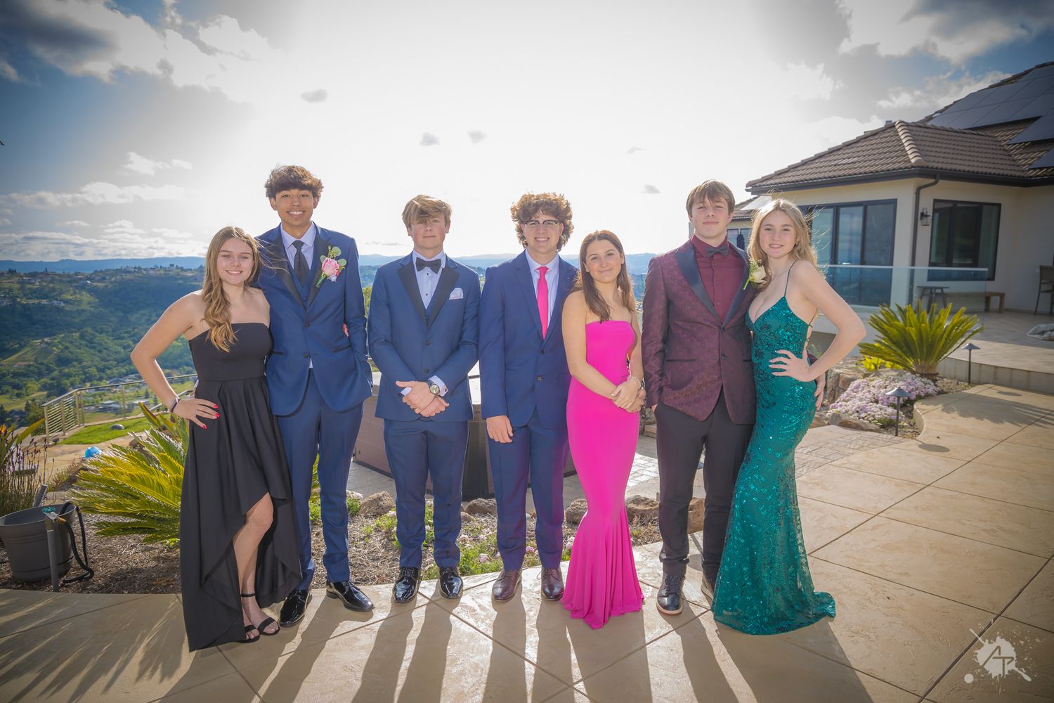 Formal group photo of friends in elegant dresses and suits on a scenic mountain terrace.