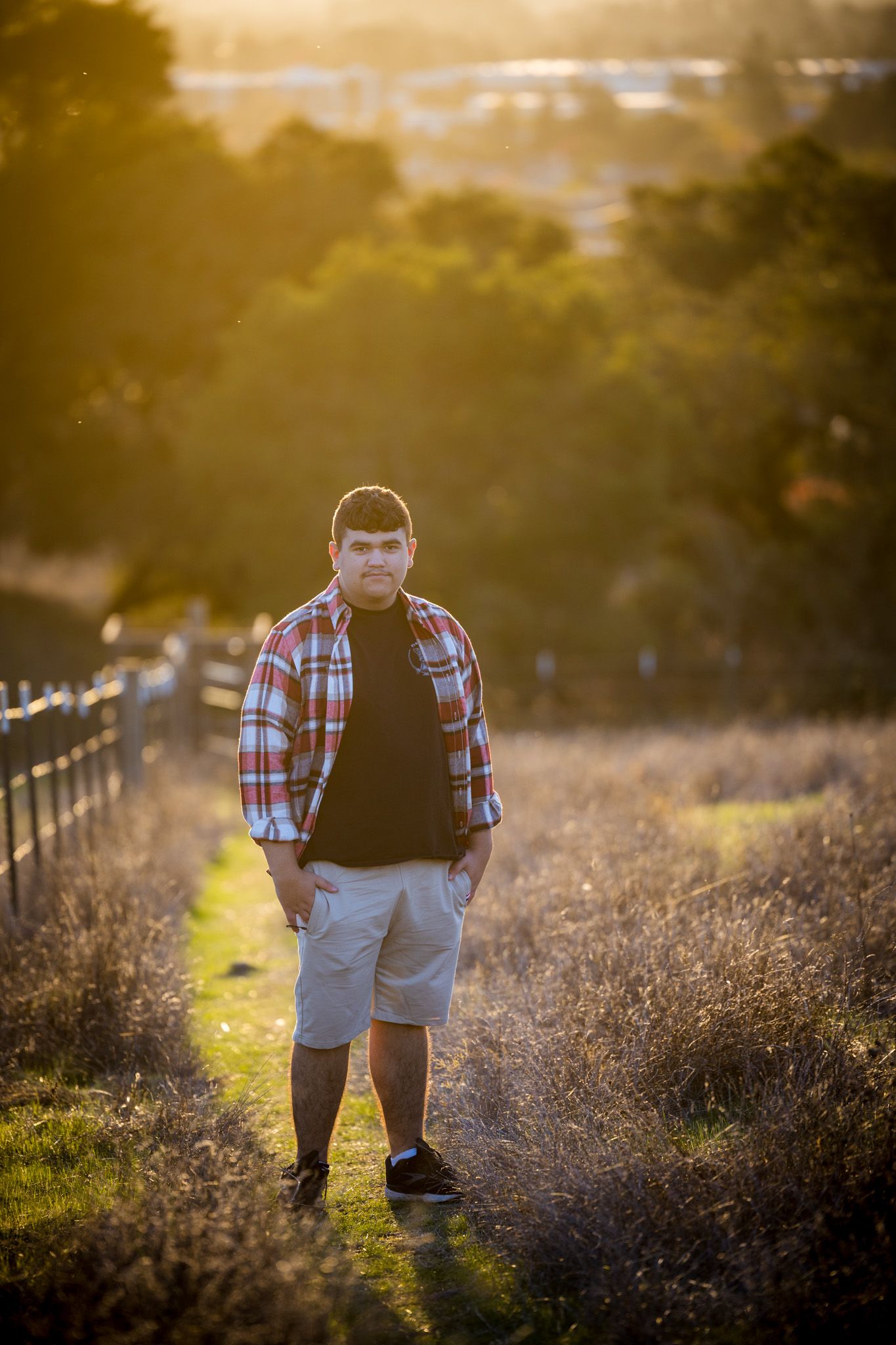 Senior Photos - Individual in plaid shirt and shorts walks along scenic trail during golden sunset.