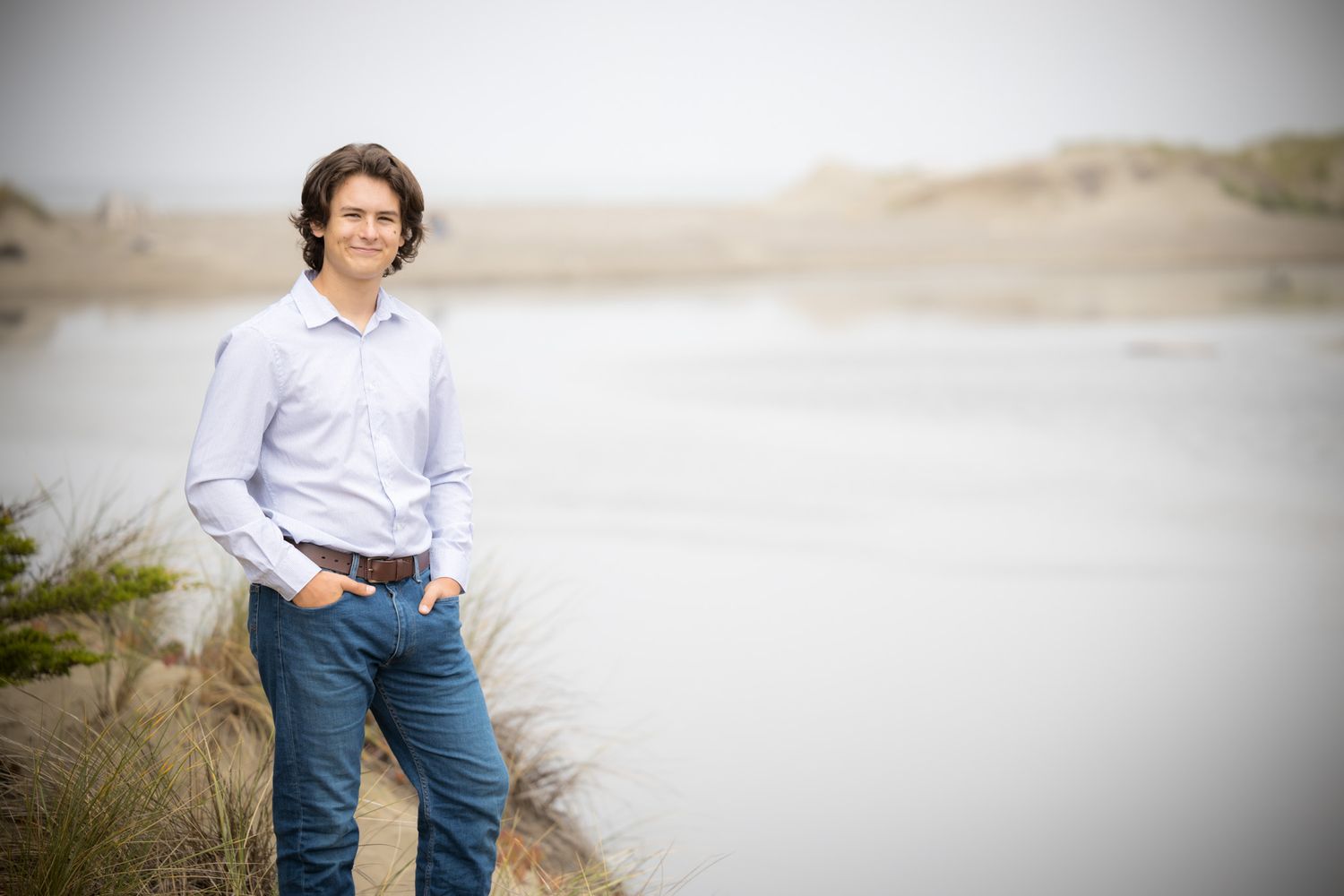 Professional portrait session against soft coastal backdrop wearing light button-down shirt and jeans.