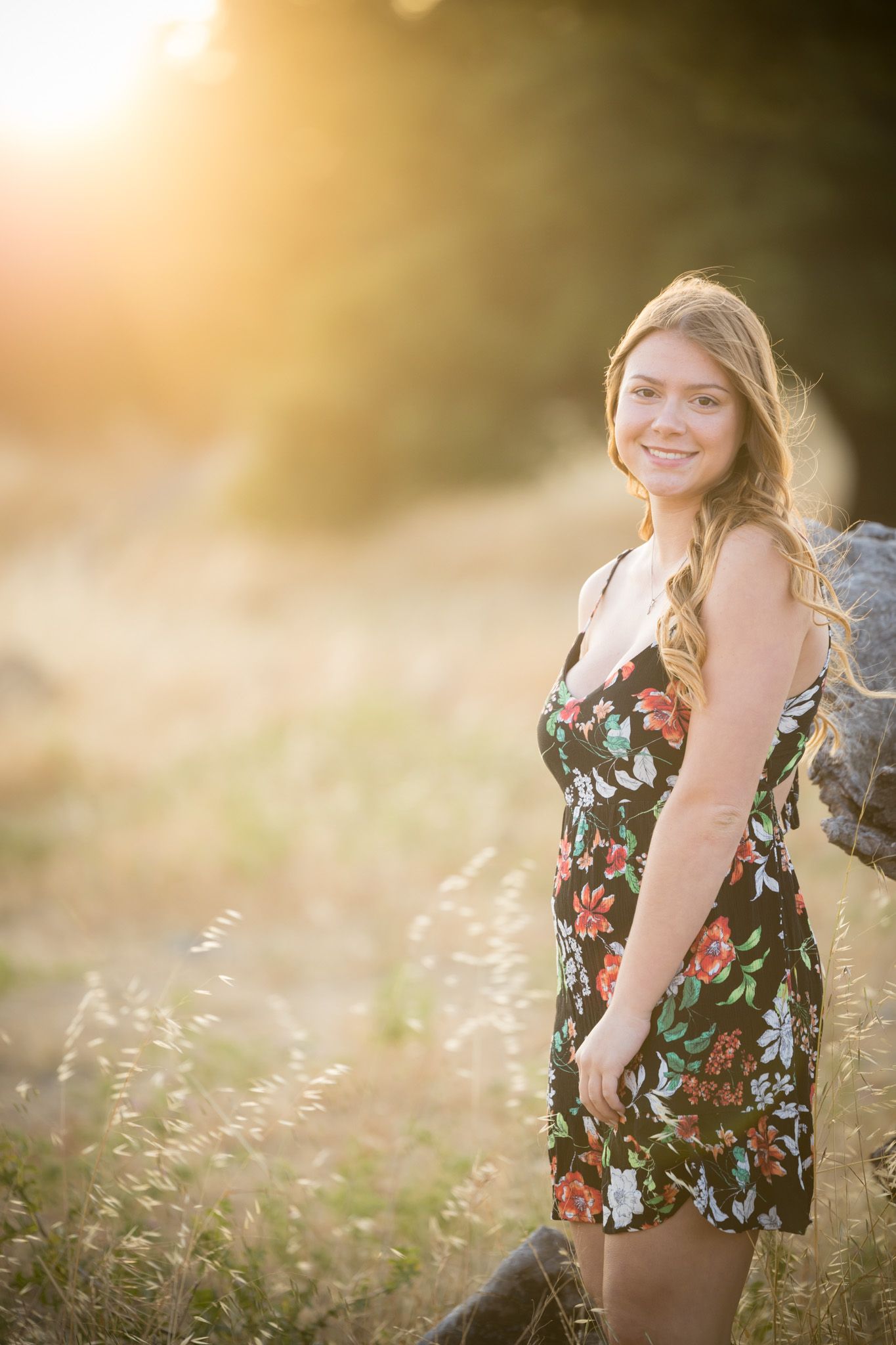 Summer portrait in floral dress against glowing sunset and golden field.