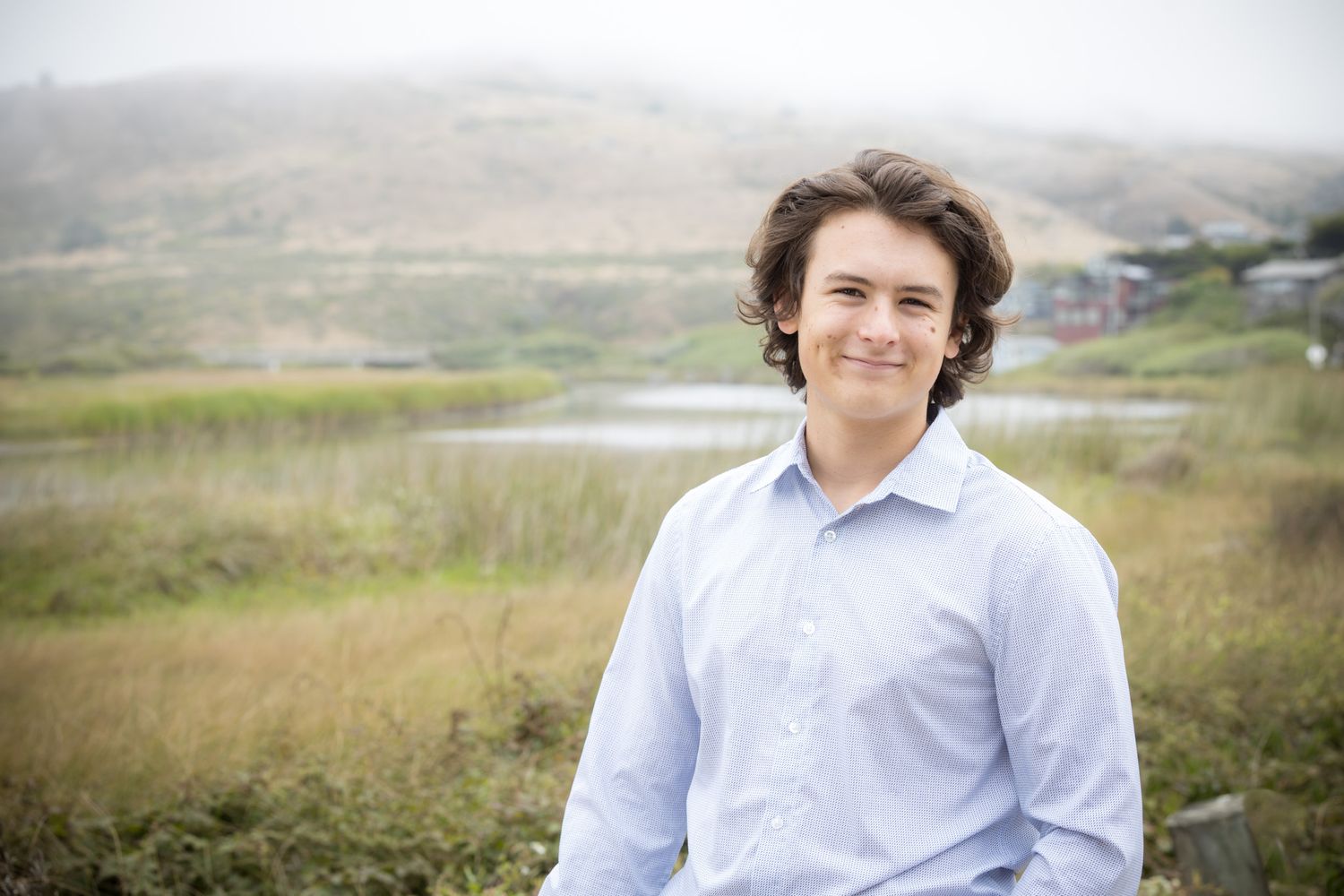 Professional headshot of person in light blue shirt against coastal landscape.