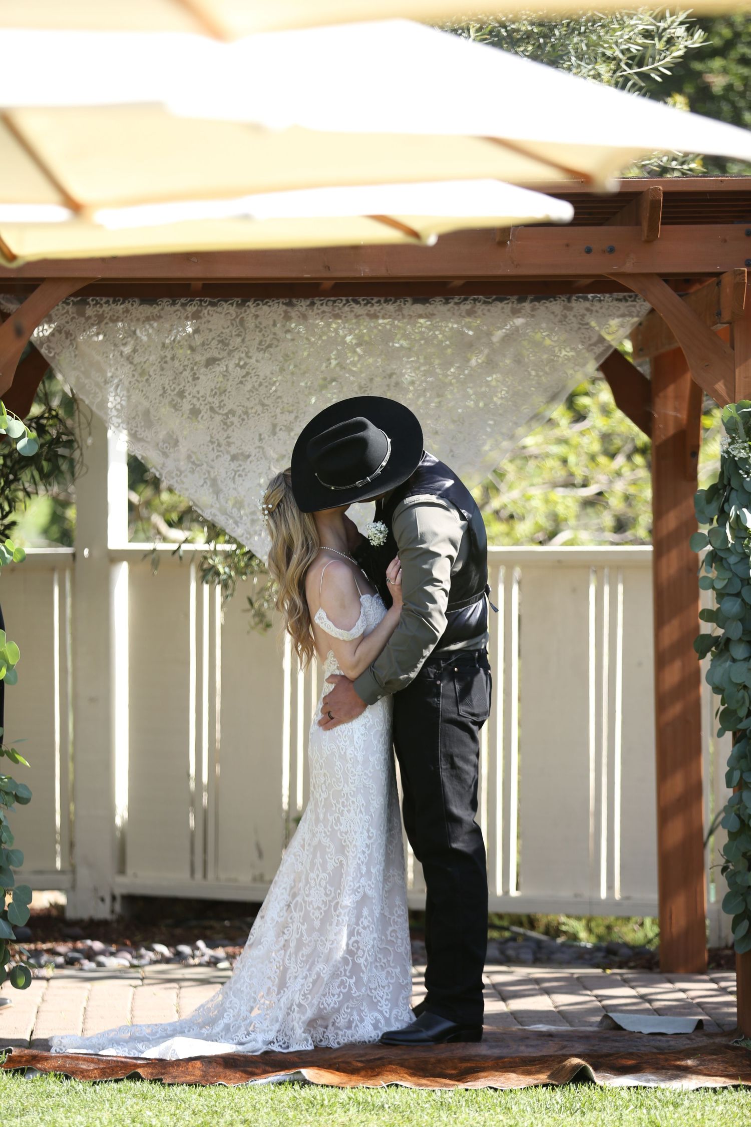 Couple embraces under a wooden gazebo decorated with crystals on their wedding day.