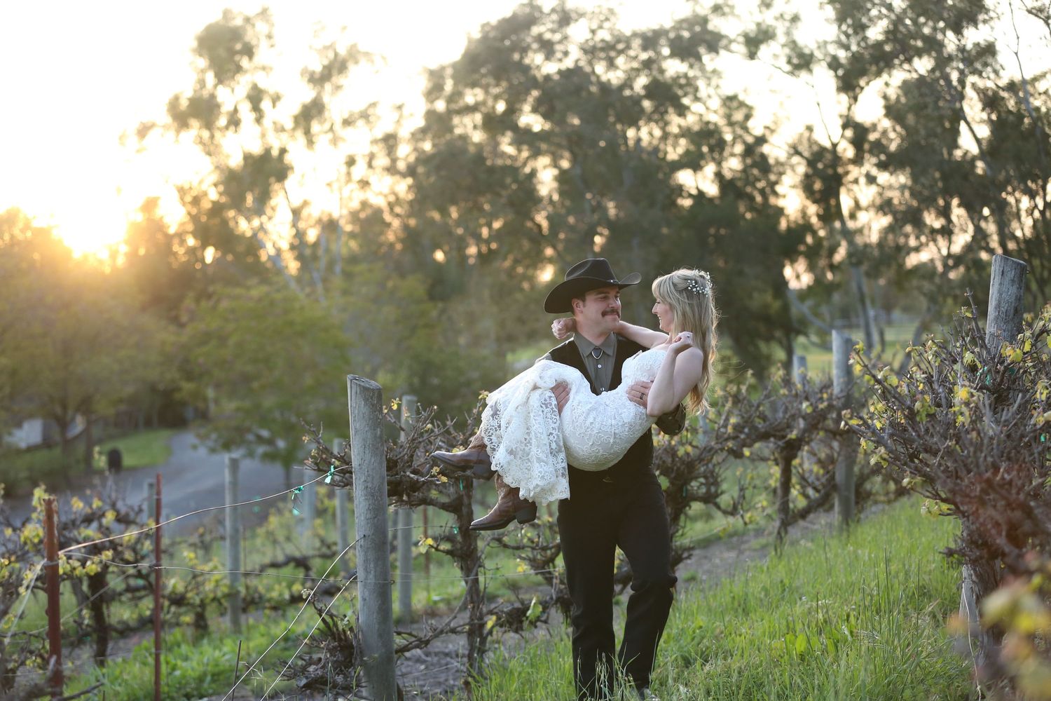 A couple shares a romantic moment in a vineyard at sunset among dormant grapevines and rolling hills.