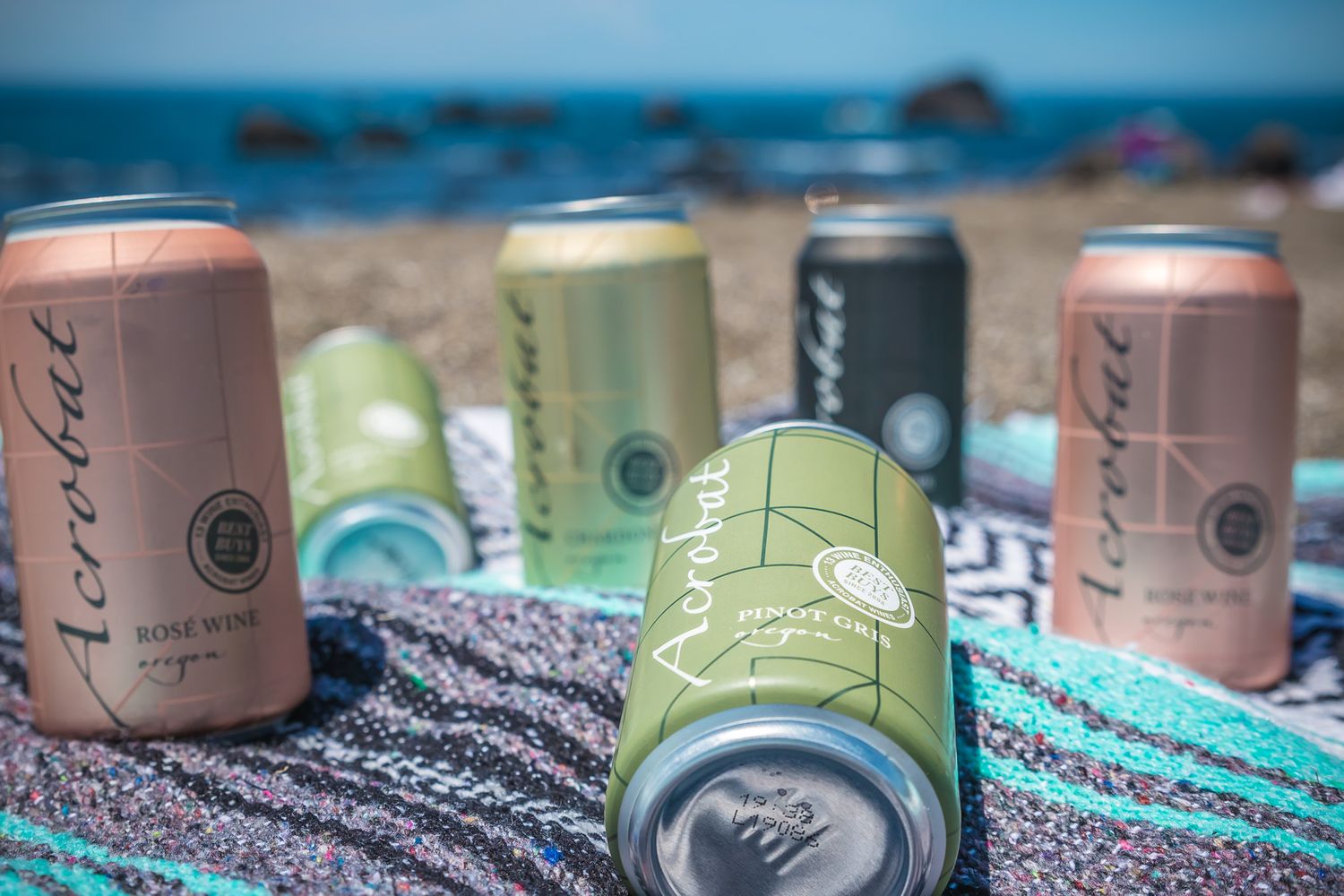 Assorted canned beverages arranged on a beach blanket near the ocean.