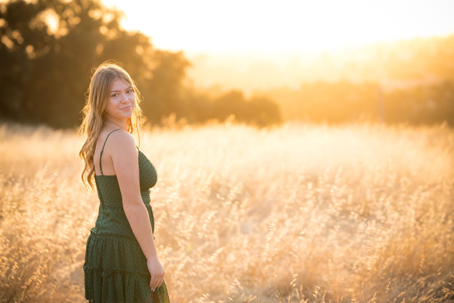 Candid outdoor portrait in green dress with golden sunlit meadow backdrop.