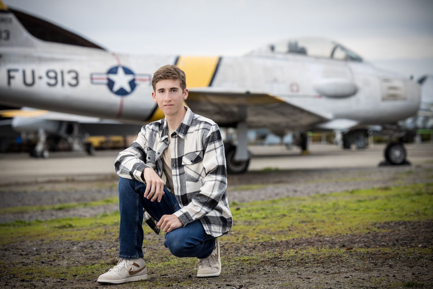 Senior Photos - Crouching pose by vintage US Air Force plane on display at airfield.