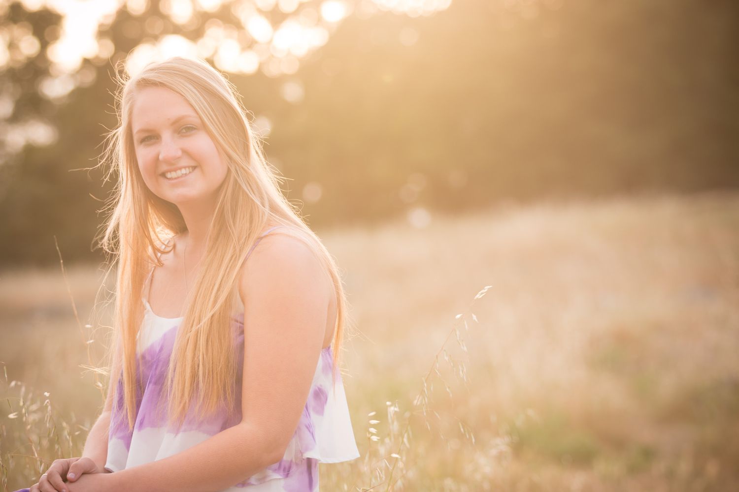 A dreamy golden hour portrait of a person sitting in a field of wildflowers at sunset.