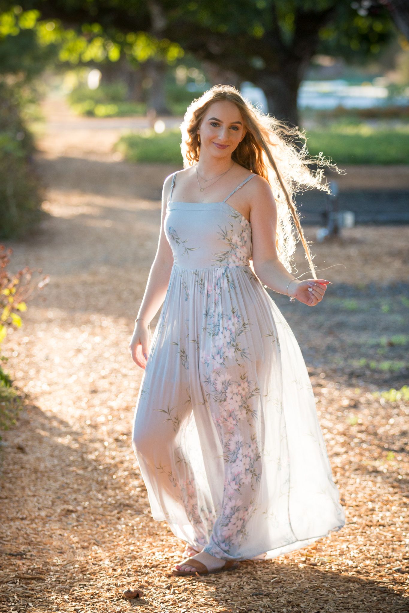 Figure twirls in a delicate white floral dress amid golden sunlit autumn leaves during an outdoor photoshoot.