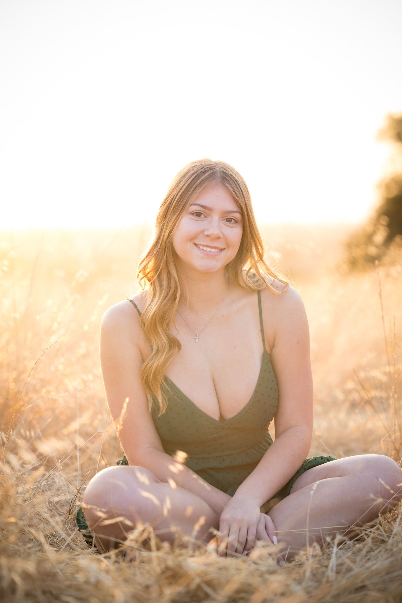 Casual summer portrait sitting in sun-drenched field wearing olive green dress.