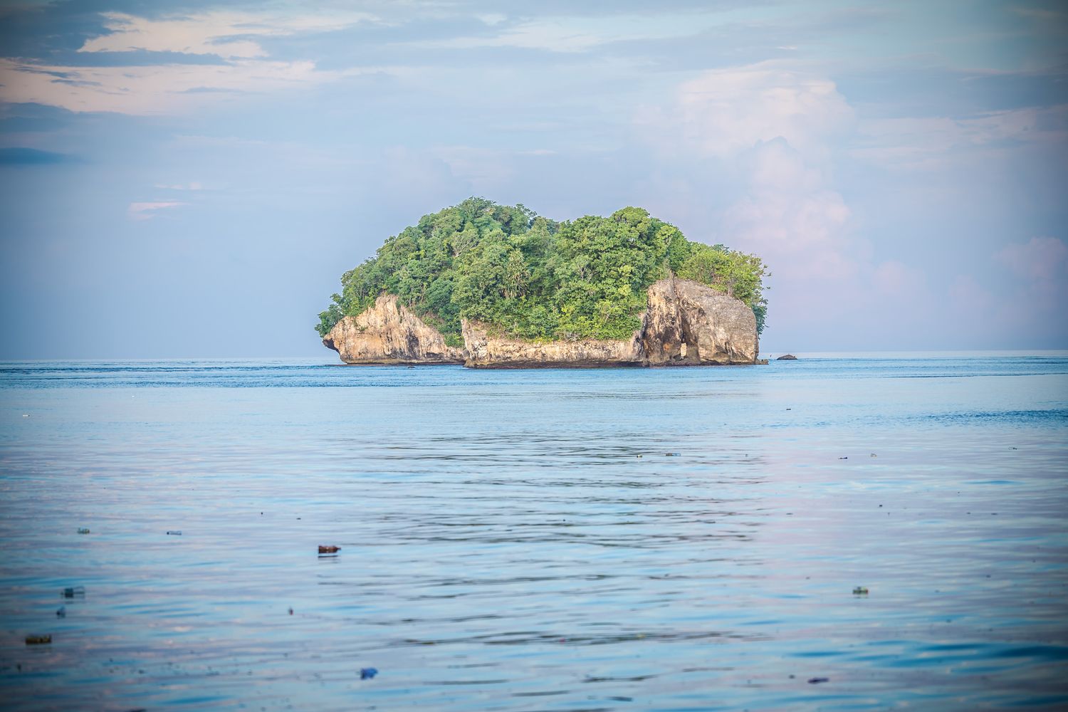 Panoramic seascape with small rocky island visible on calm blue waters.