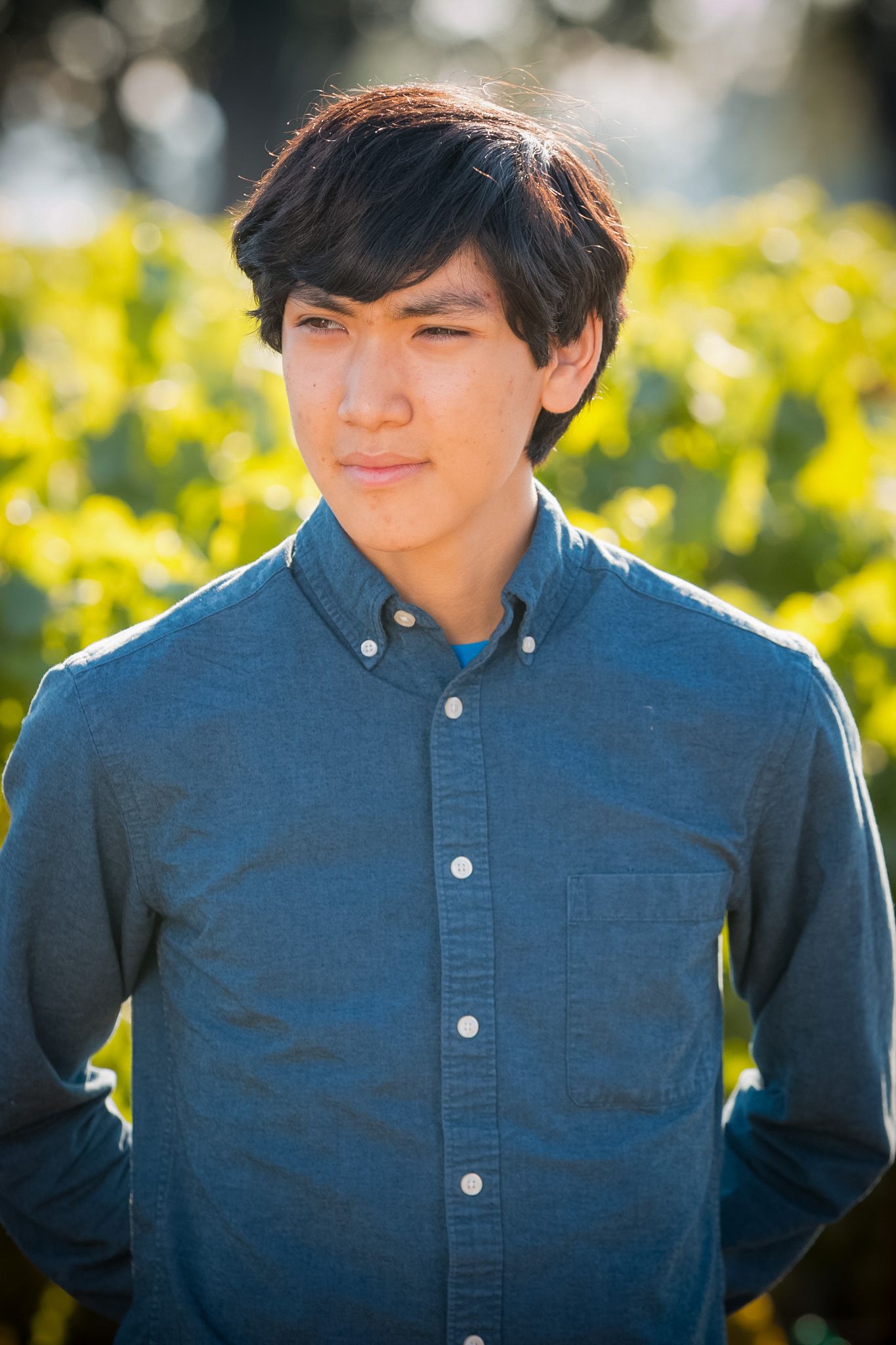 Casual outdoor portrait with sunlit vineyard backdrop.